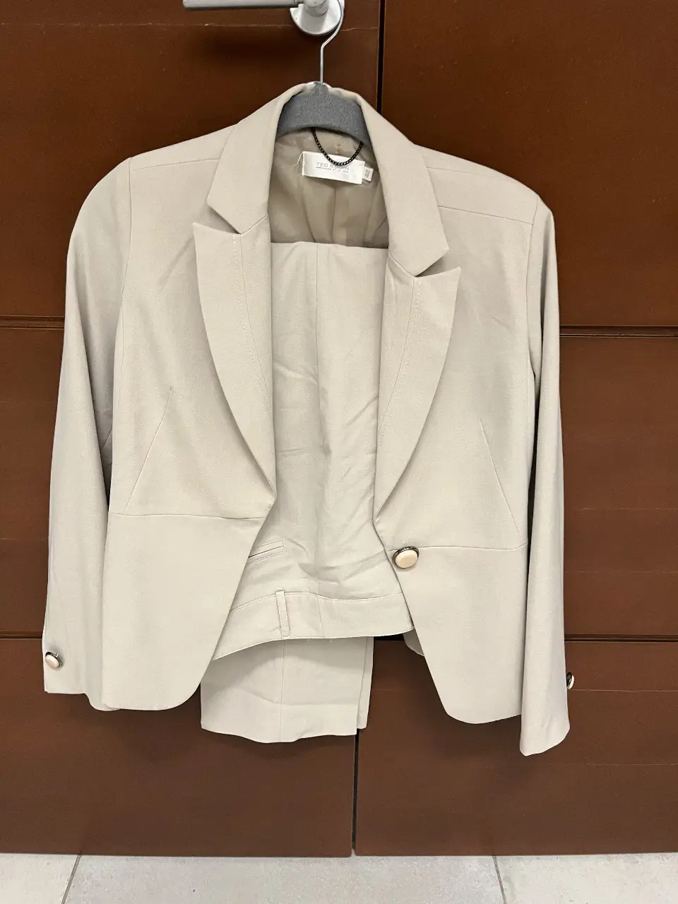 Traje sastrero color crudo, compuesto por blazer con botones dorados y pantalón a juego. Ideal para un look formal y elegante.