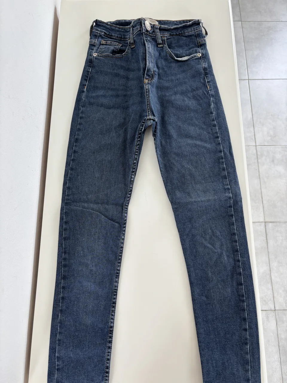 Jean de tiro alto, color azul oscuro, con detalles de costuras y bolsillos.