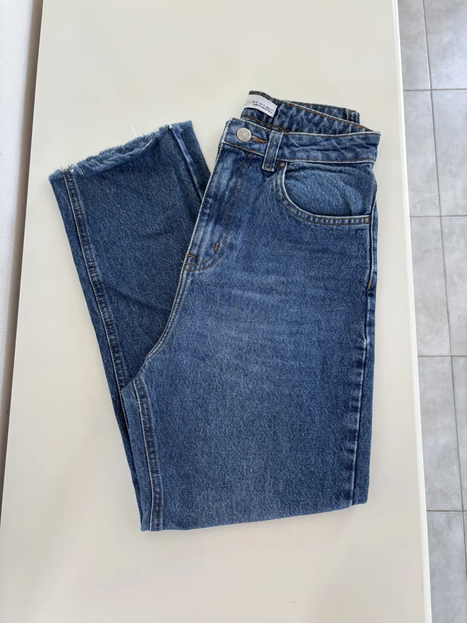 Jeans de tiro alto con desflecado en los bordes inferiores. Color azul clásico con desgaste.