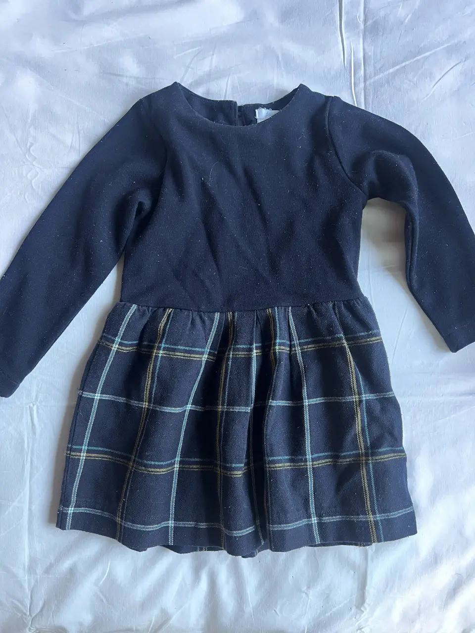 Vestido de niña, manga larga, con cuerpo azul marino y falda a cuadros en tonos azul, amarillo y verde. Ideal para el día a día.