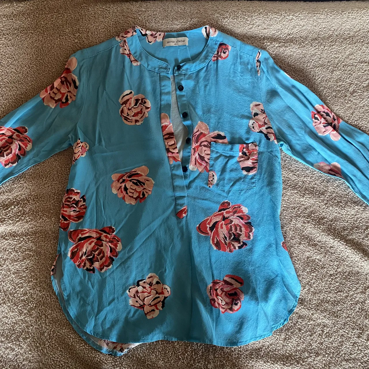 Remera manga larga azul vibrante con estampa floral de rosas en tonos rosas y rojos. Cuello mao con botones y un bolsillo en el frente. Ideal para un look casual y fresco.