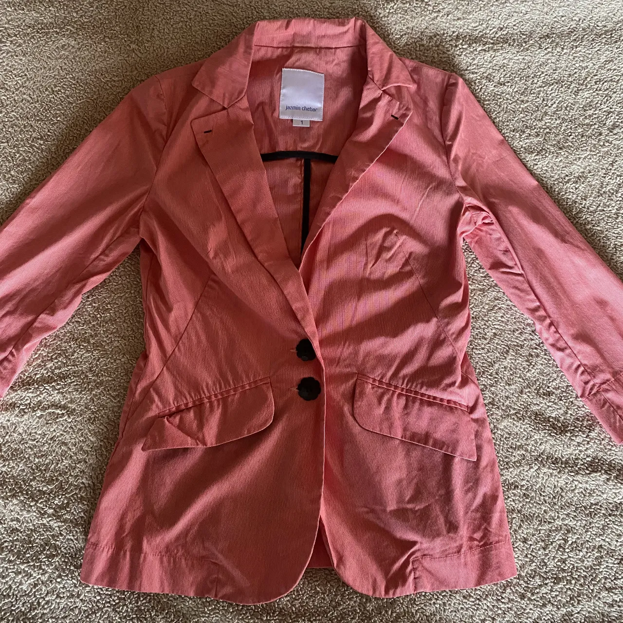 Blazer rosa a rayas finas, con dos botones negros al frente y bolsillos con solapa. Ideal para un look elegante y moderno.