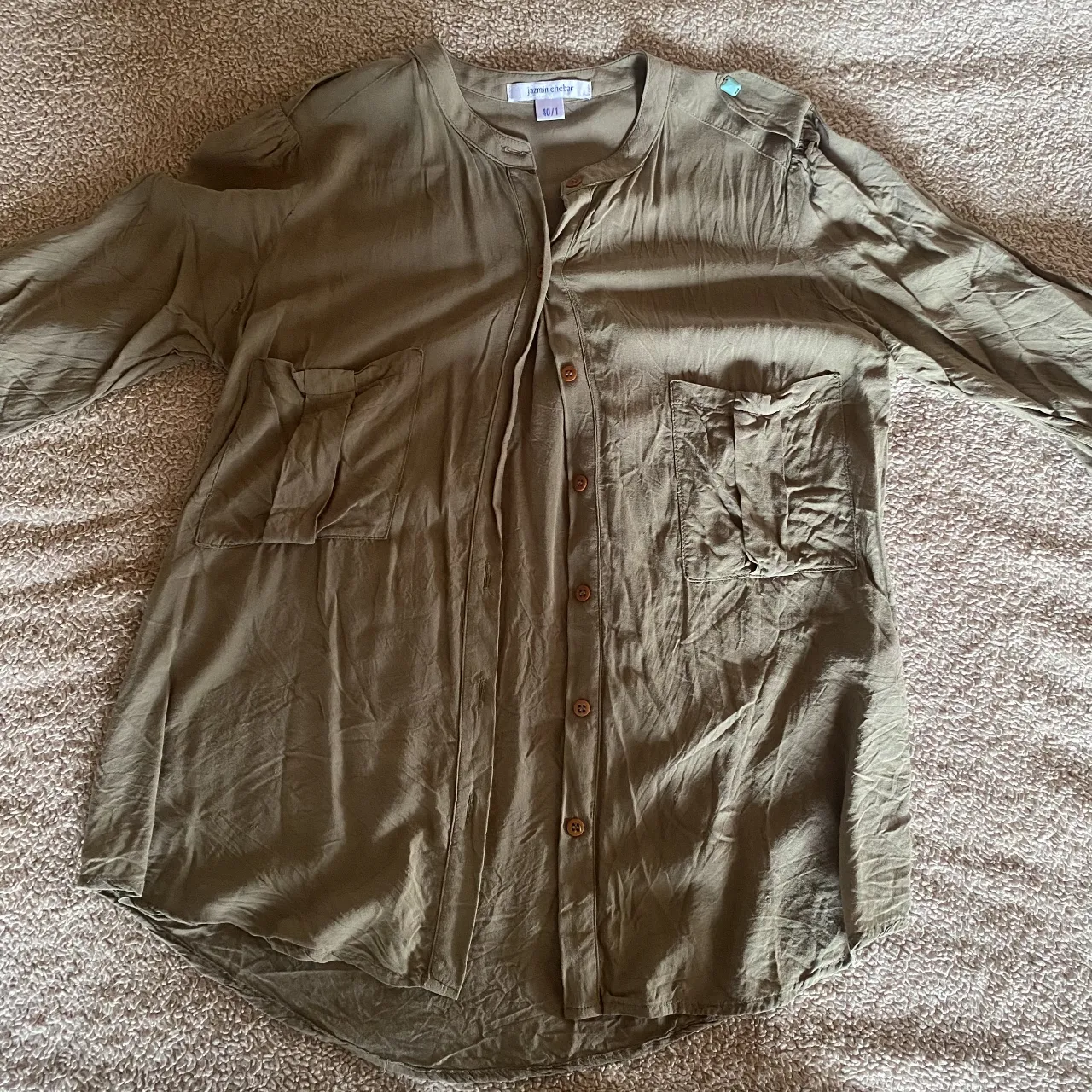 Camisa de manga larga en color verde militar, con cuello mao y botones al frente. Posee dos bolsillos con solapa en el pecho y detalles de costura en los laterales. Ideal para un look casual y moderno.