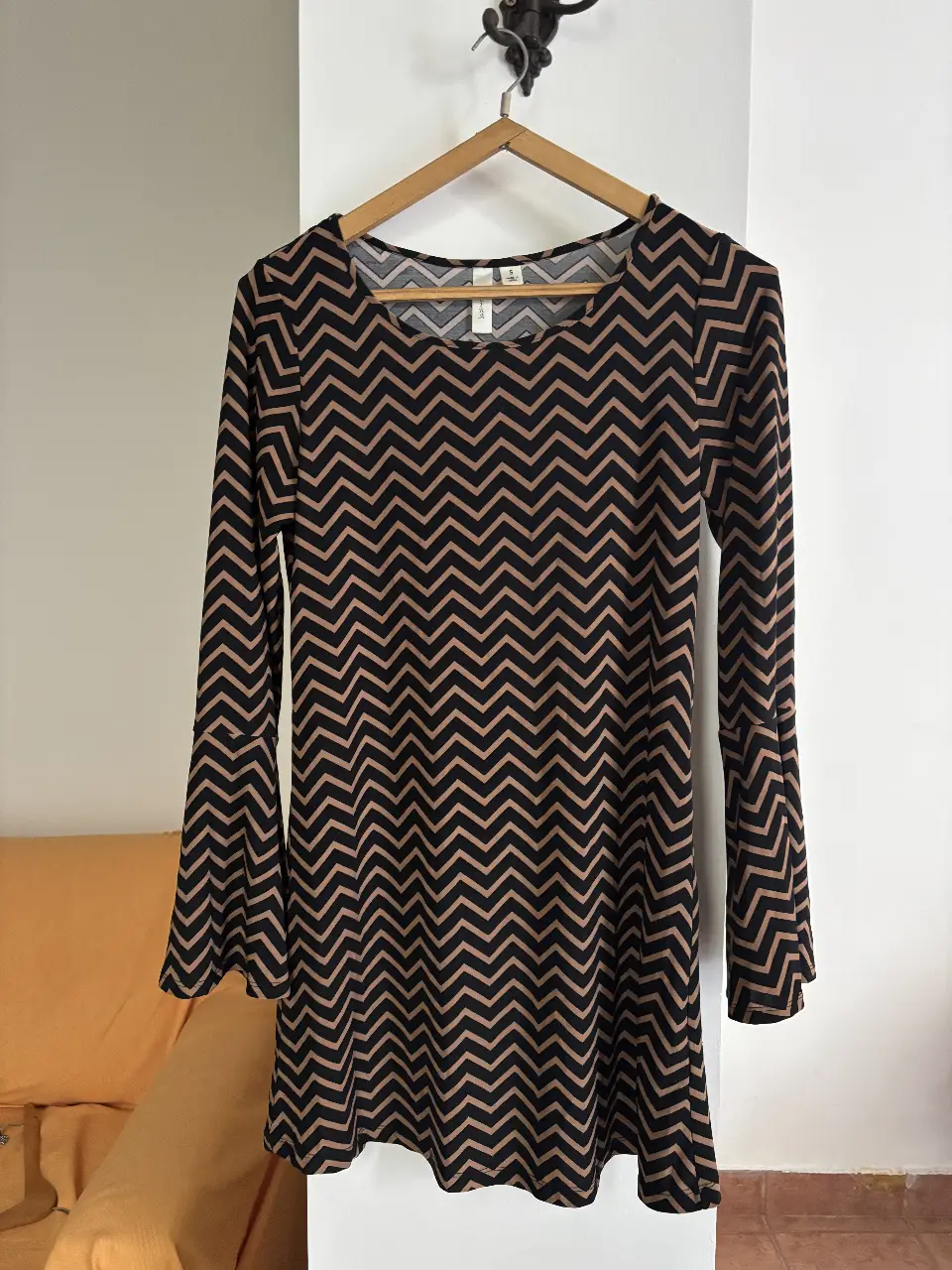 Vestido midi con estampado de chevron en negro y marrón. Mangas largas con volados en los puños. Ideal para un look elegante y moderno.