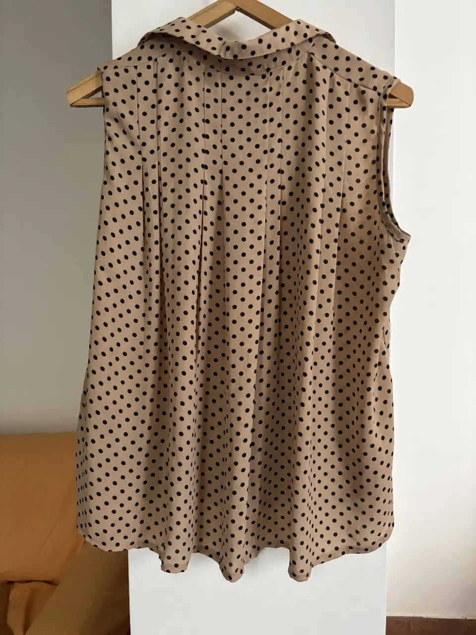 Blusa sin mangas para mujer, con estampado de lunares negros sobre fondo crudo. Diseño con cuello camisero y botones frontales. Ideal para un look casual y elegante.