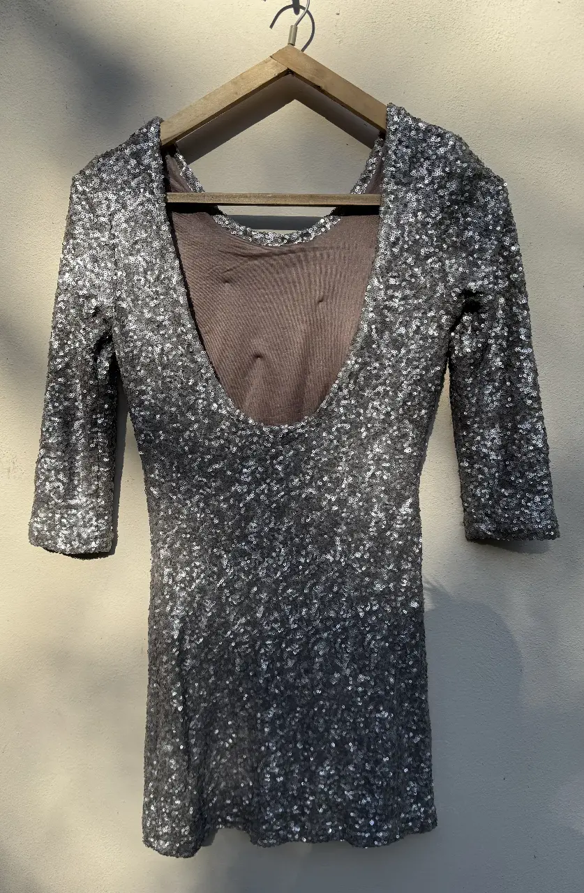Vestido mini de fiesta con lentejuelas plateadas. Ideal para eventos especiales y salidas nocturnas. Diseño con espalda descubierta y mangas 3/4.