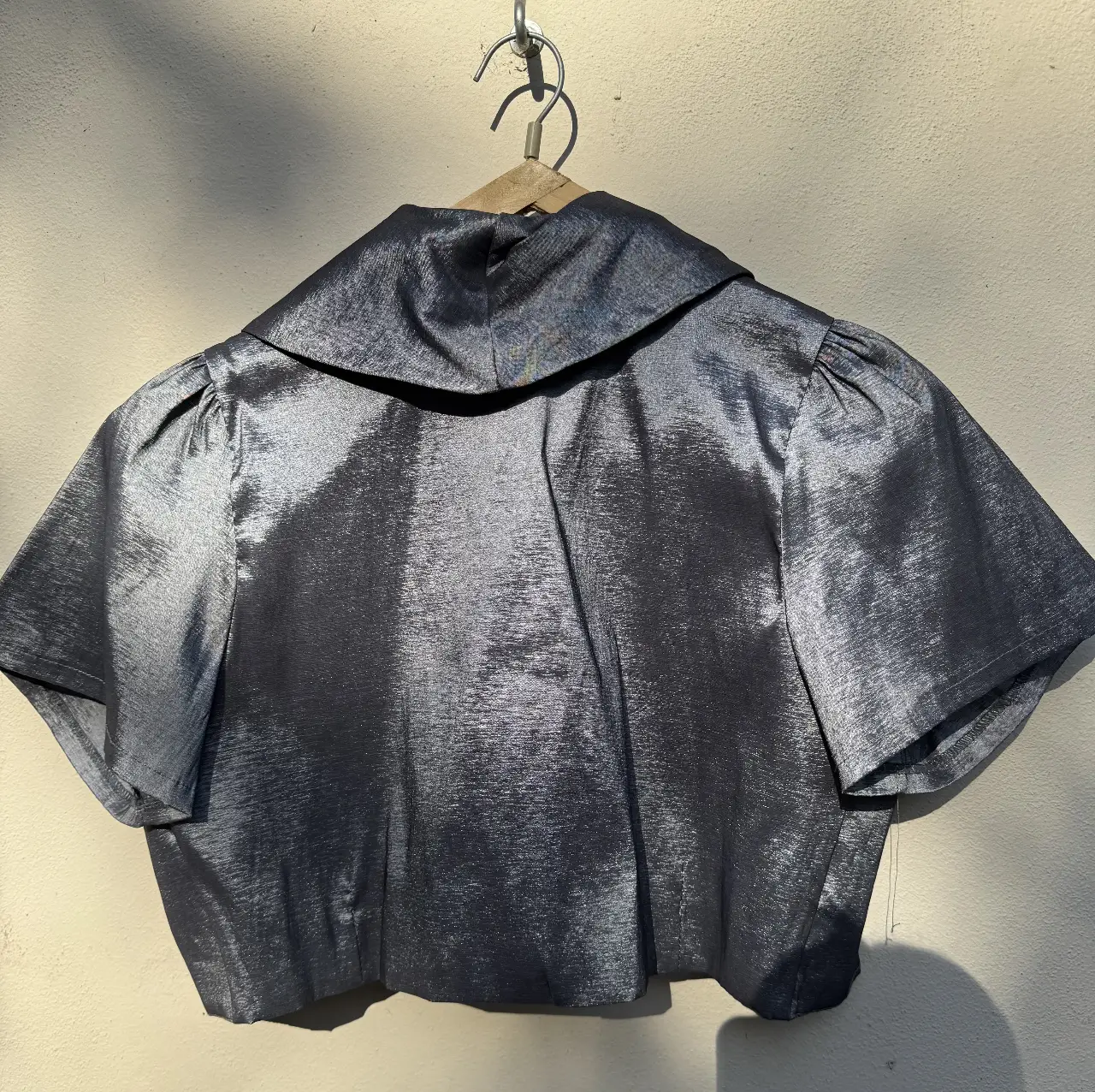 Blusa bolero plateada con mangas cortas abullonadas y cuello solapa. Ideal para eventos formales o para darle un toque elegante a tu look.