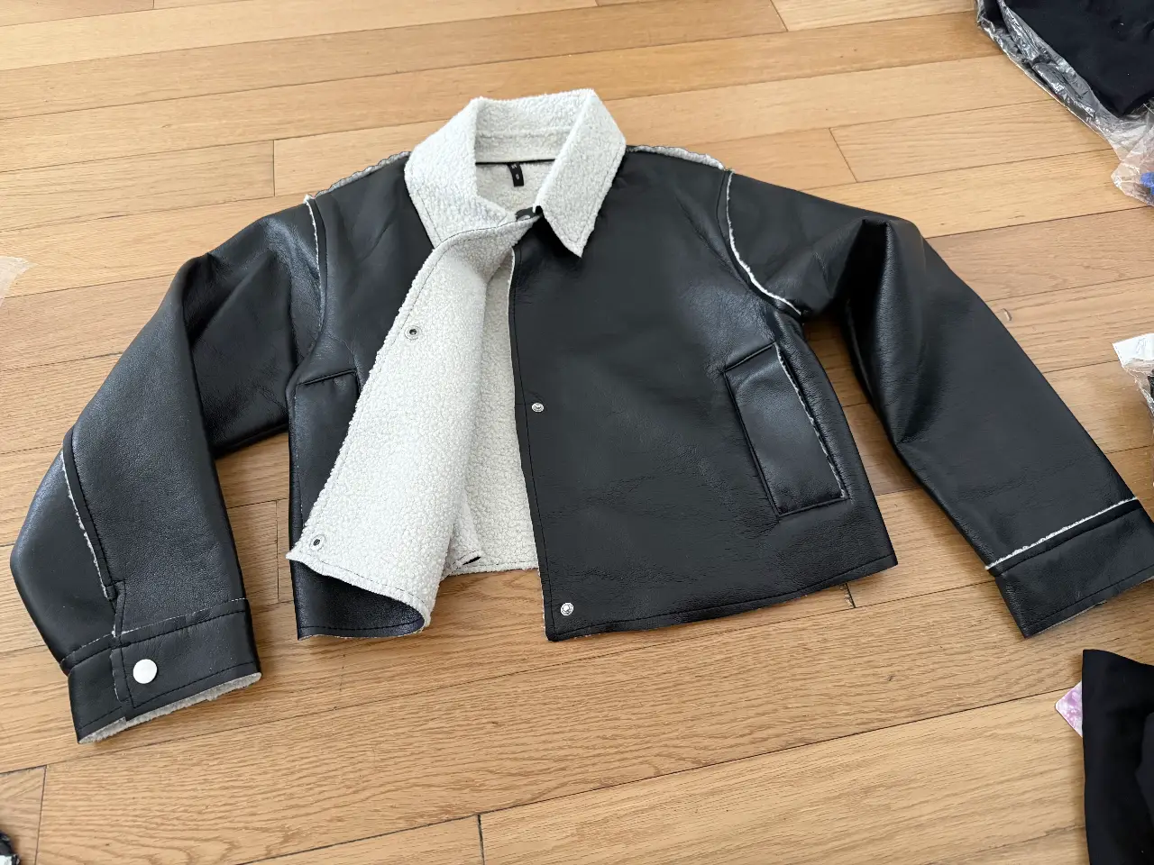 Campera de cuero sintético negra con interior de piel sintética blanca. Detalles de costuras blancas y bolsillos. Ideal para un look moderno y abrigado.