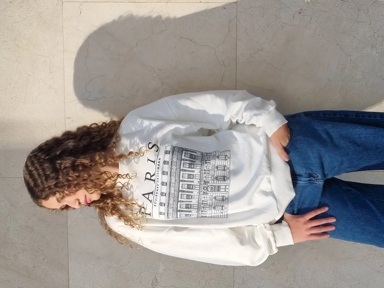 Buzo de cuello redondo blanco con estampado "PARIS" y un diseño de un edificio. Ideal para un look casual y cómodo.