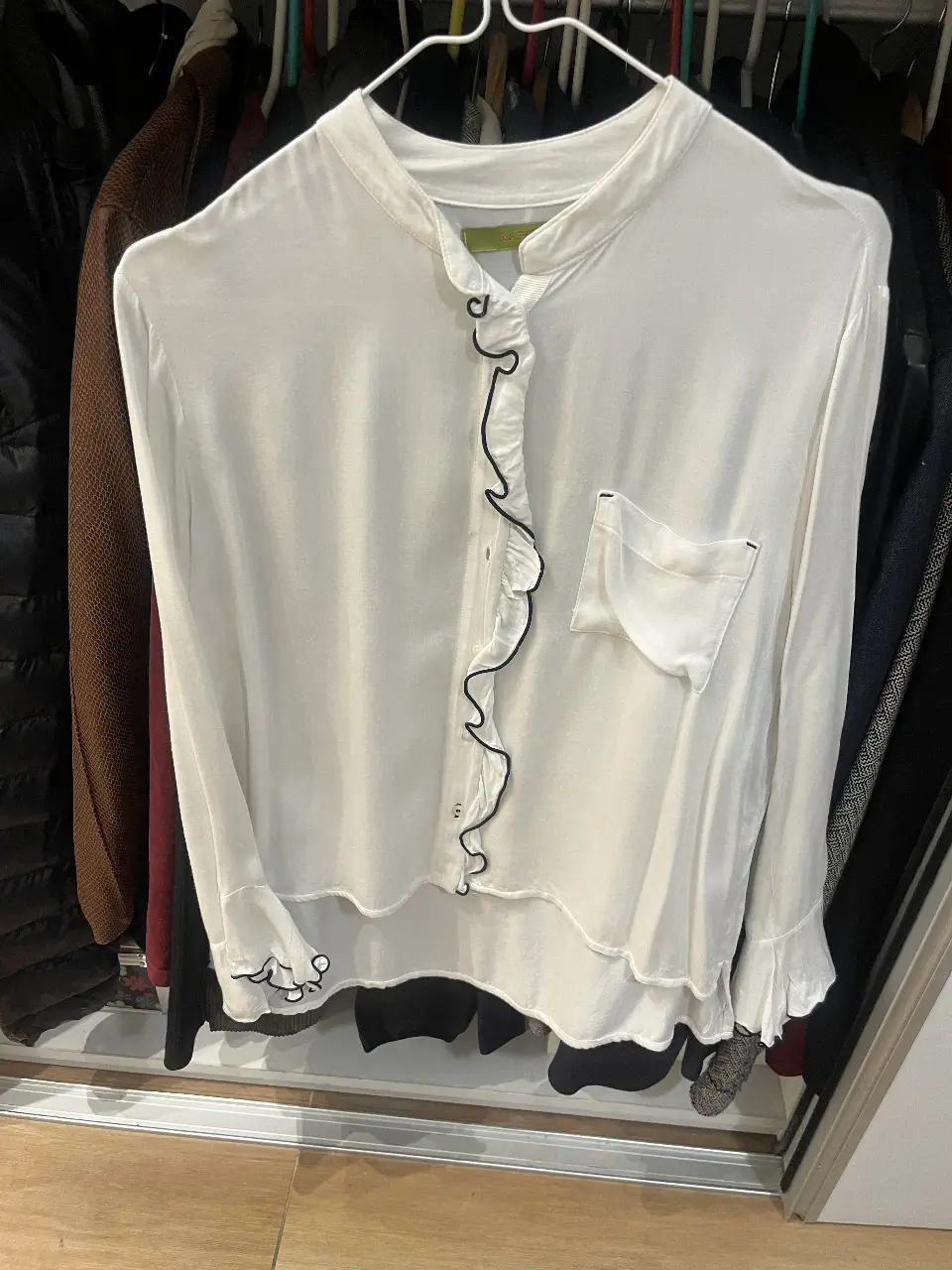 Blusa blanca de mujer, con detalle de volados en el frente y puños con bordado negro. Cuello mao y bolsillo en el pecho. Marca Rapsodia.