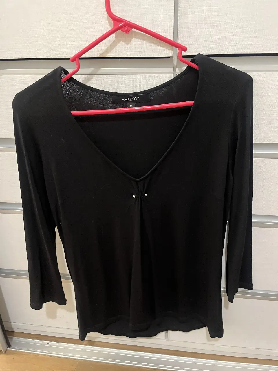 Blusa negra de manga 3/4 con escote en V y detalles delicados. Ideal para un look elegante y versátil.