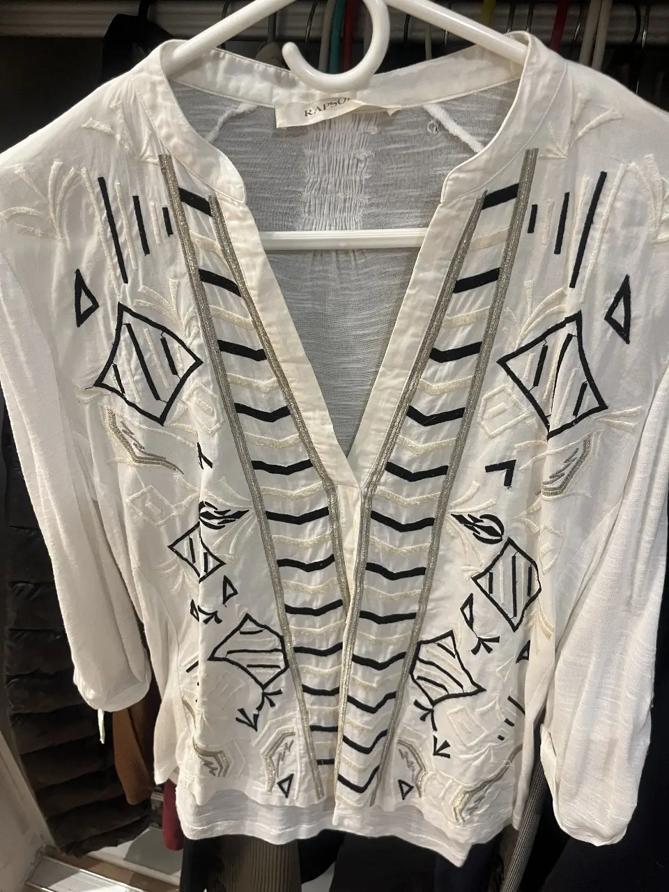 Blusa blanca con detalles bordados en negro y dorado, estilo boho. Ideal para un look casual y fresco.