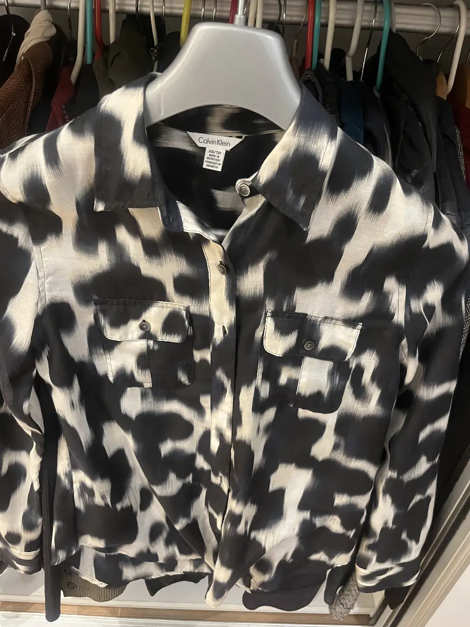 Camisa estampada Calvin Klein en blanco y negro, con estampado de manchas. Talle XS/TP. Ideal para un look casual o de trabajo.