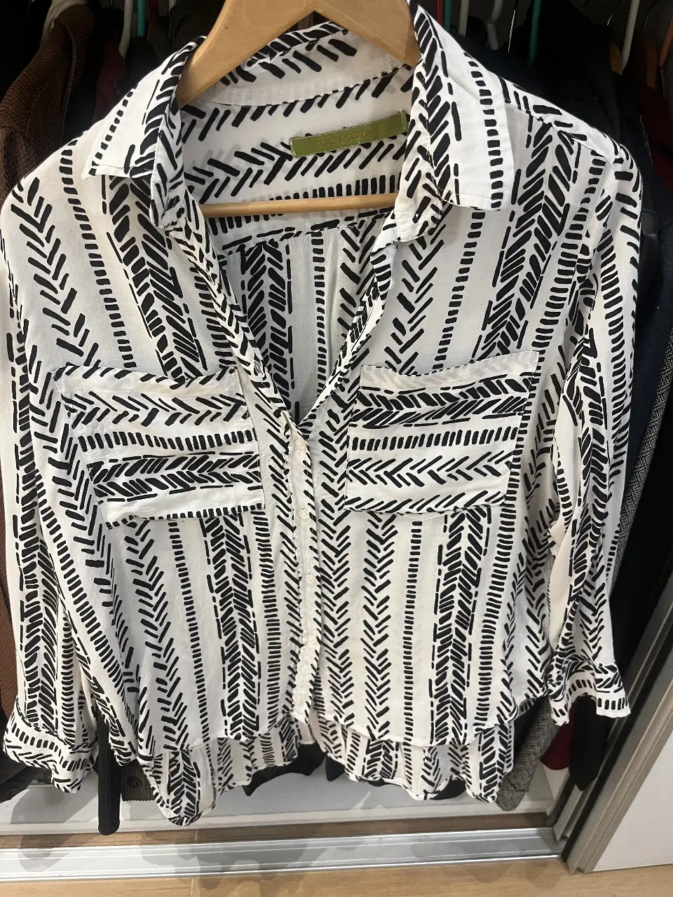 Camisa estampada de mujer, con diseño de líneas negras sobre fondo blanco. la parte de atrás es más larga y finaliza con un volado. Marca Rapsodia. Ideal para un look casual y moderno.