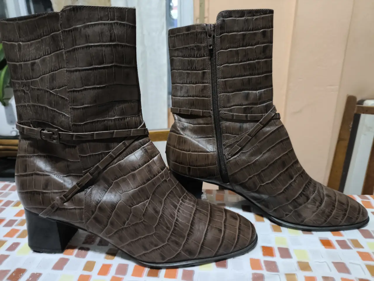 Botas de caña alta de cuero marrón con diseño de cocodrilo. Tienen un detalle de correa con hebilla y cierre lateral. Ideales para un look elegante y sofisticado.