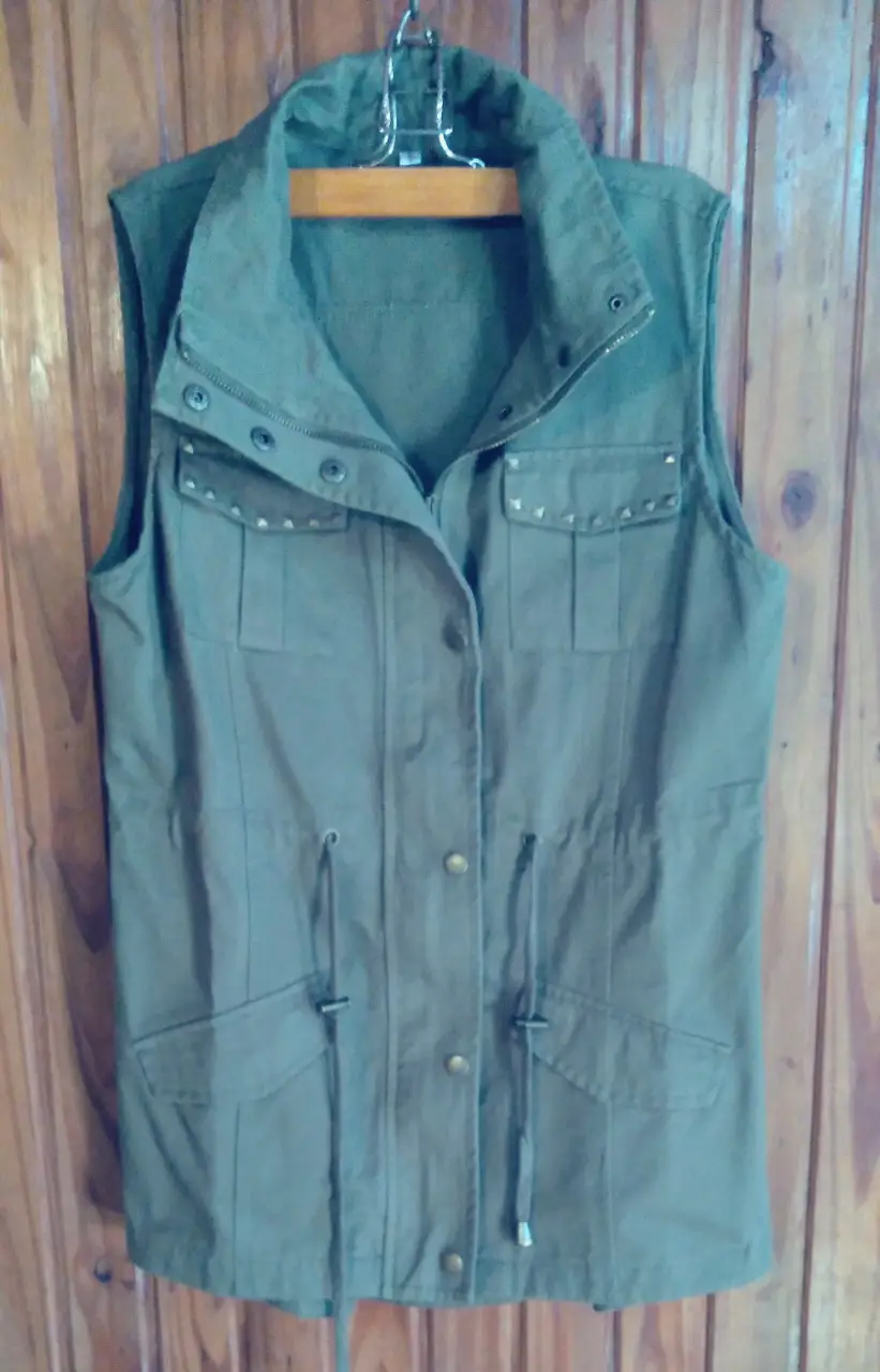 Chaleco verde militar con detalles de tachas en los bolsillos. Posee cierre y botones, además de cordones ajustables en la cintura. Ideal para un look casual y canchero.