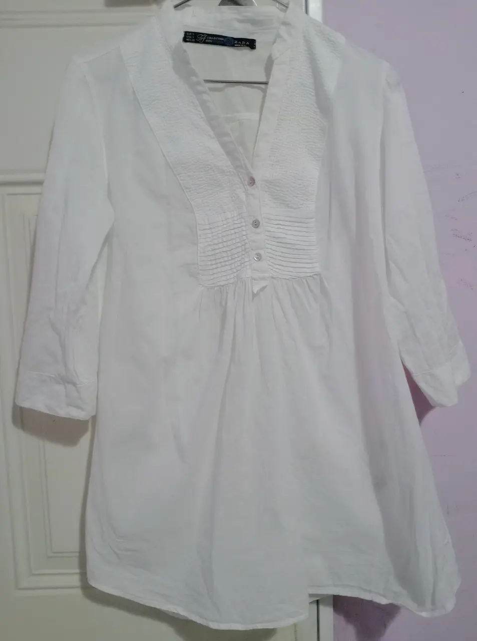Blusa blanca de mujer, con cuello en V y detalles plisados en el frente. Manga 3/4. Ideal para un look elegante y fresco.