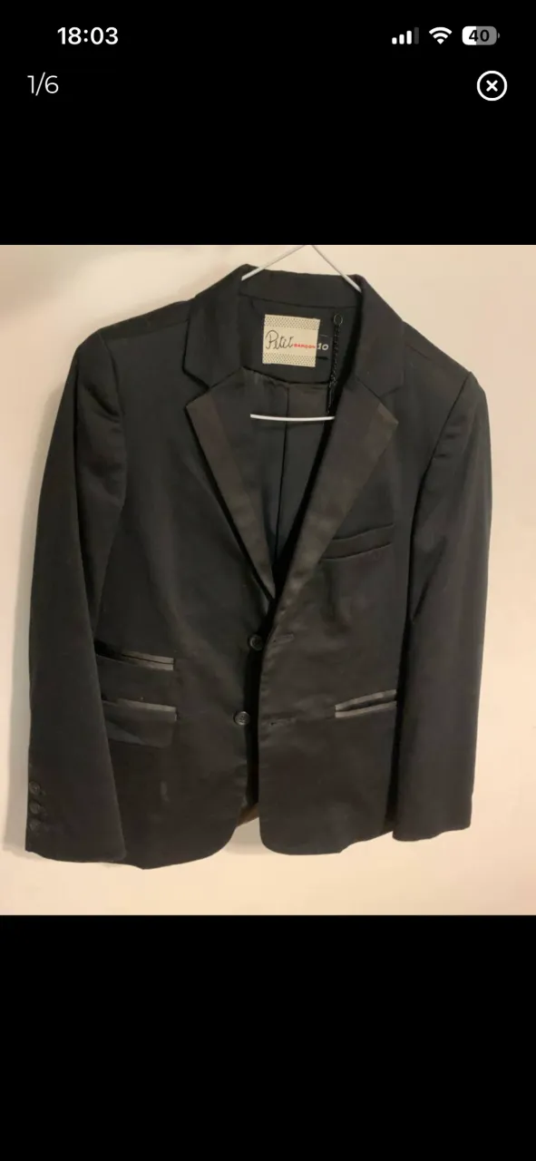 Blazer negro de vestir con solapa de satén y dos botones frontales. Posee bolsillos con tapa y puños con botones. Incluye funda protectora de tela. Marca Garcon Garcia Talle 10 de niño