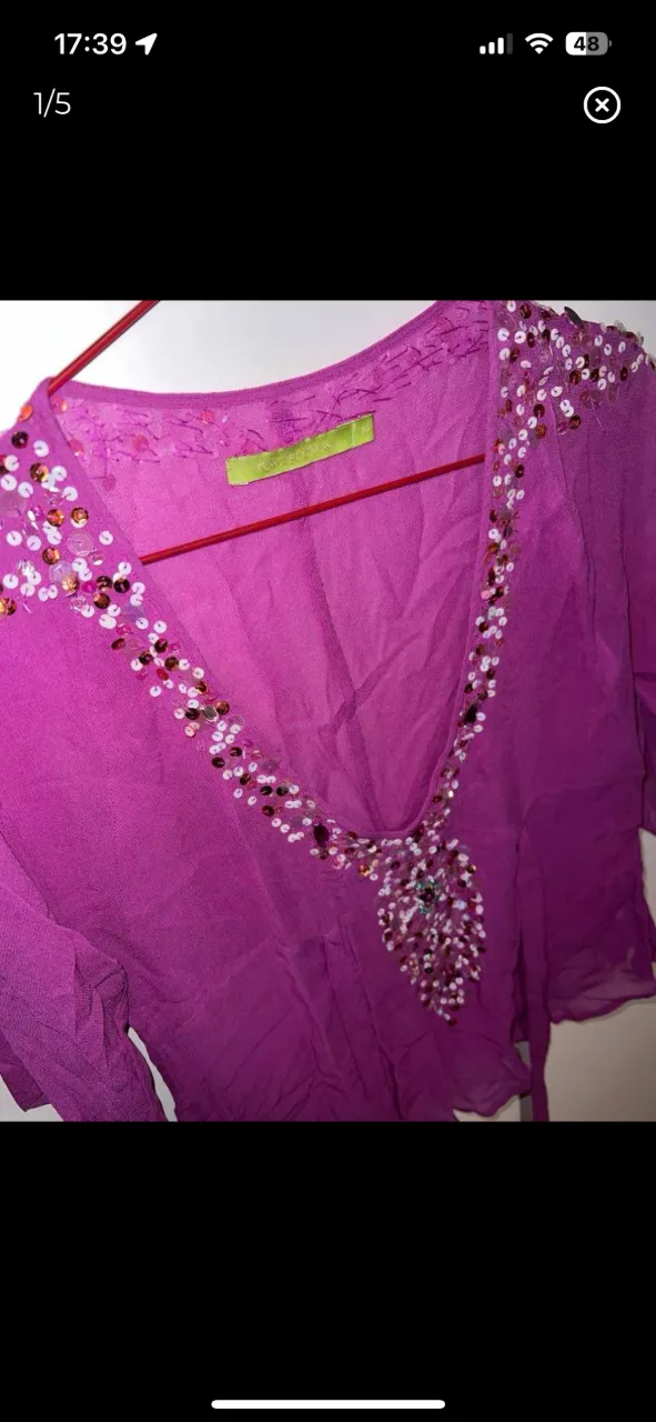 Blusa color fucsia con escote en V, manga corta y detalles de lentejuelas y canutillos bordados en el escote y hombros. Posee lazos para atar en la cintura.