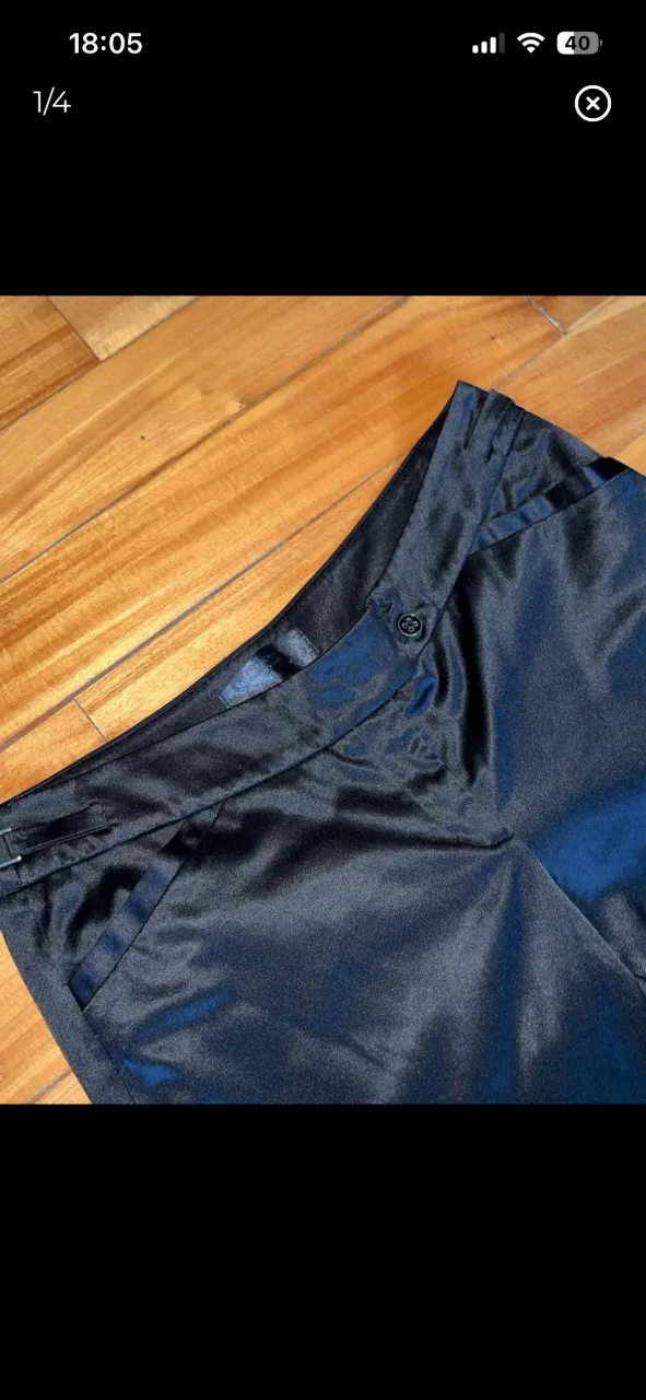 Pantalón negro de tela satinada con bolsillos delanteros y un botón en la cintura. Tiro Bajo marca Markova
