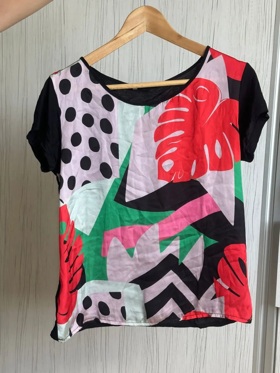 Remera súper original y colorida con estampa abstracta y hojas tropicales. Mangas cortas negras y cuello redondo. Ideal para darle un toque divertido a tu look.