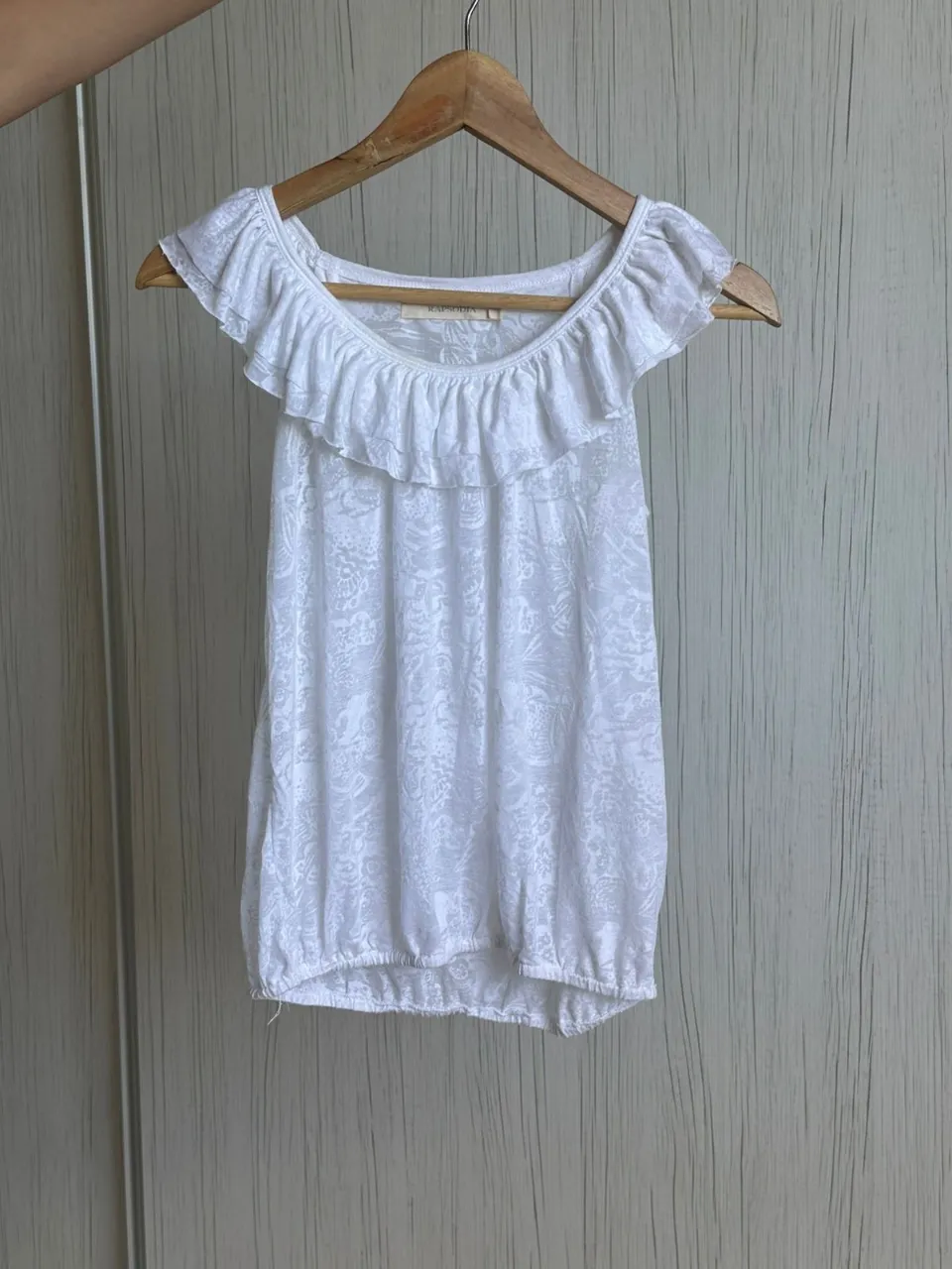 Remera blanca con volados en el cuello y mangas cortas. Posee un estampado sutil en toda la prenda. Ideal para un look casual y fresco.