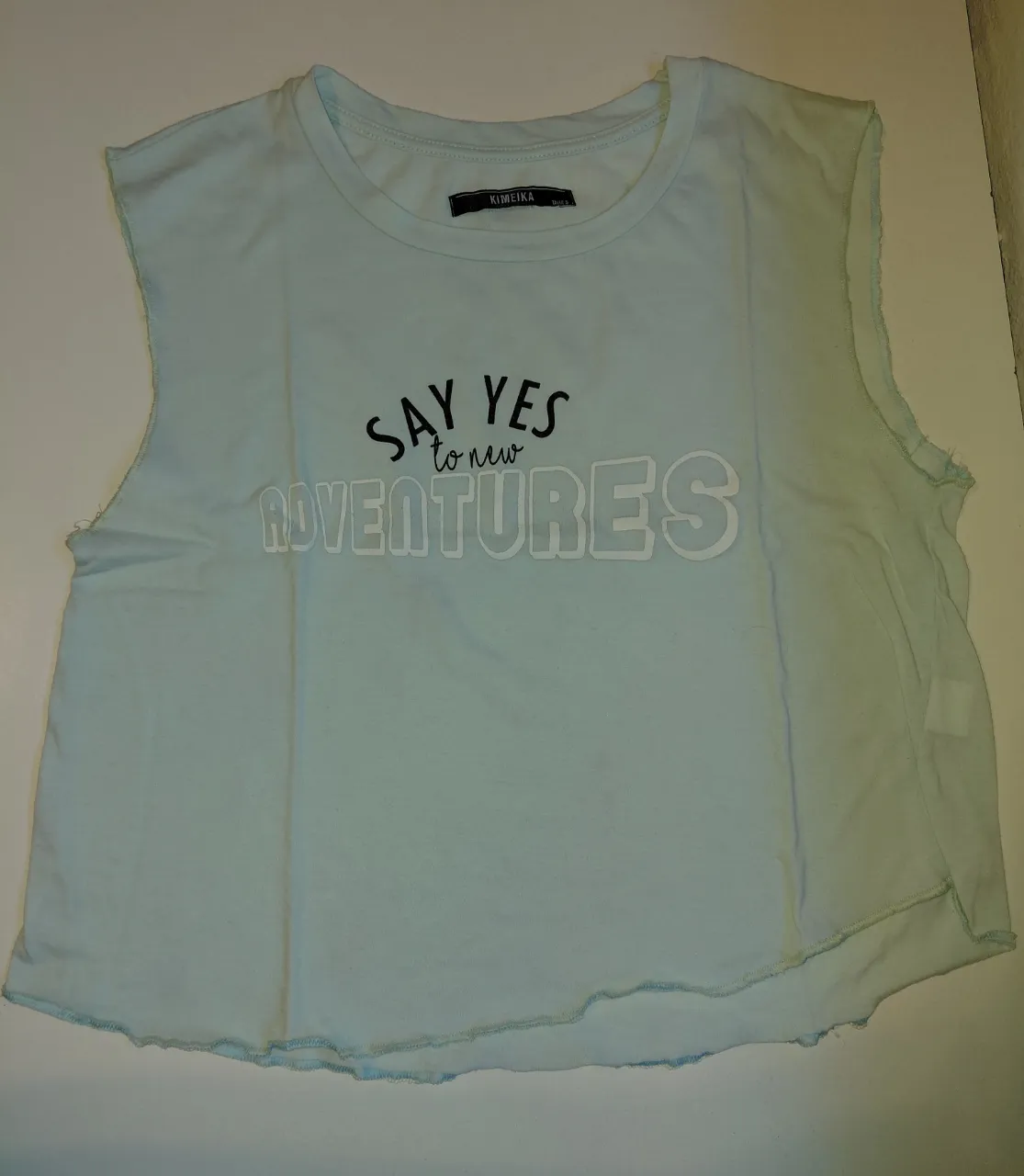 Musculosa celeste con estampa "SAY YES to new ADVENTURES". Posee los bordes deshilachados.