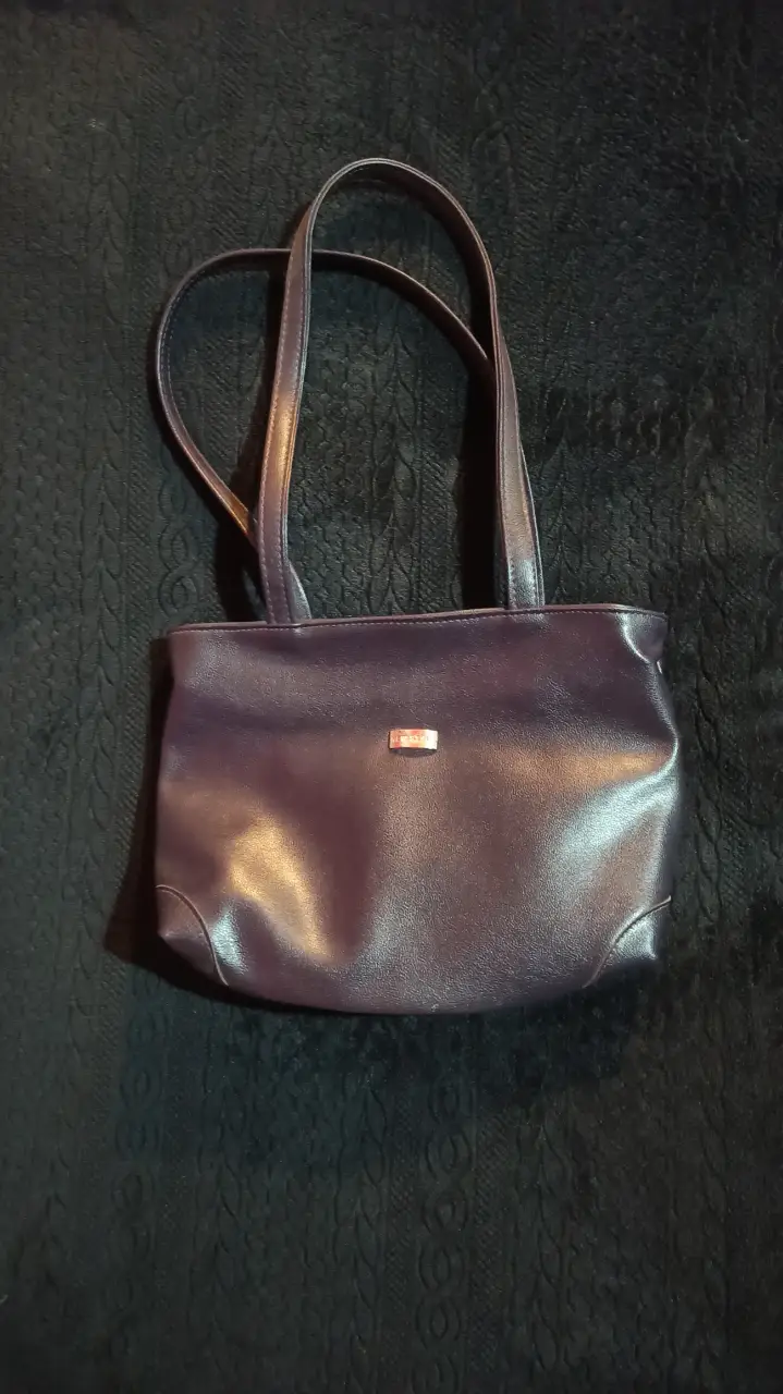 Cartera de color violeta oscuro, con manijas cortas y un pequeño detalle metálico en el frente. Ideal para un look elegante y sofisticado. buen estado sin detalles 