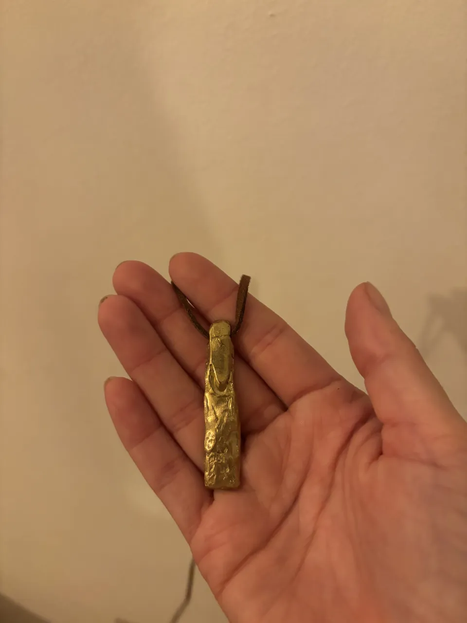 Collar con dije alargado y texturizado, de color dorado, con cordón de cuero marrón.