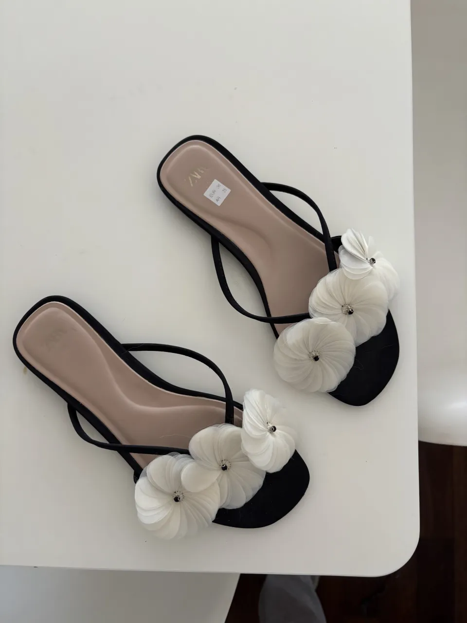 Sandalias negras con tiras finas y apliques de flores blancas en la capellada. Suela plana.