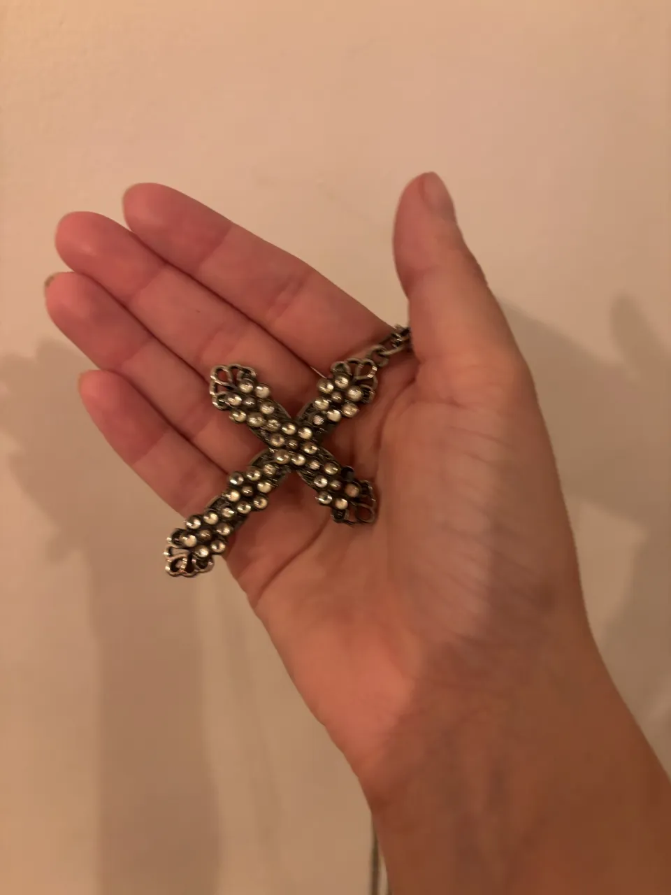 Collar con dije de cruz plateada con incrustaciones de piedras brillantes y cadena fina.