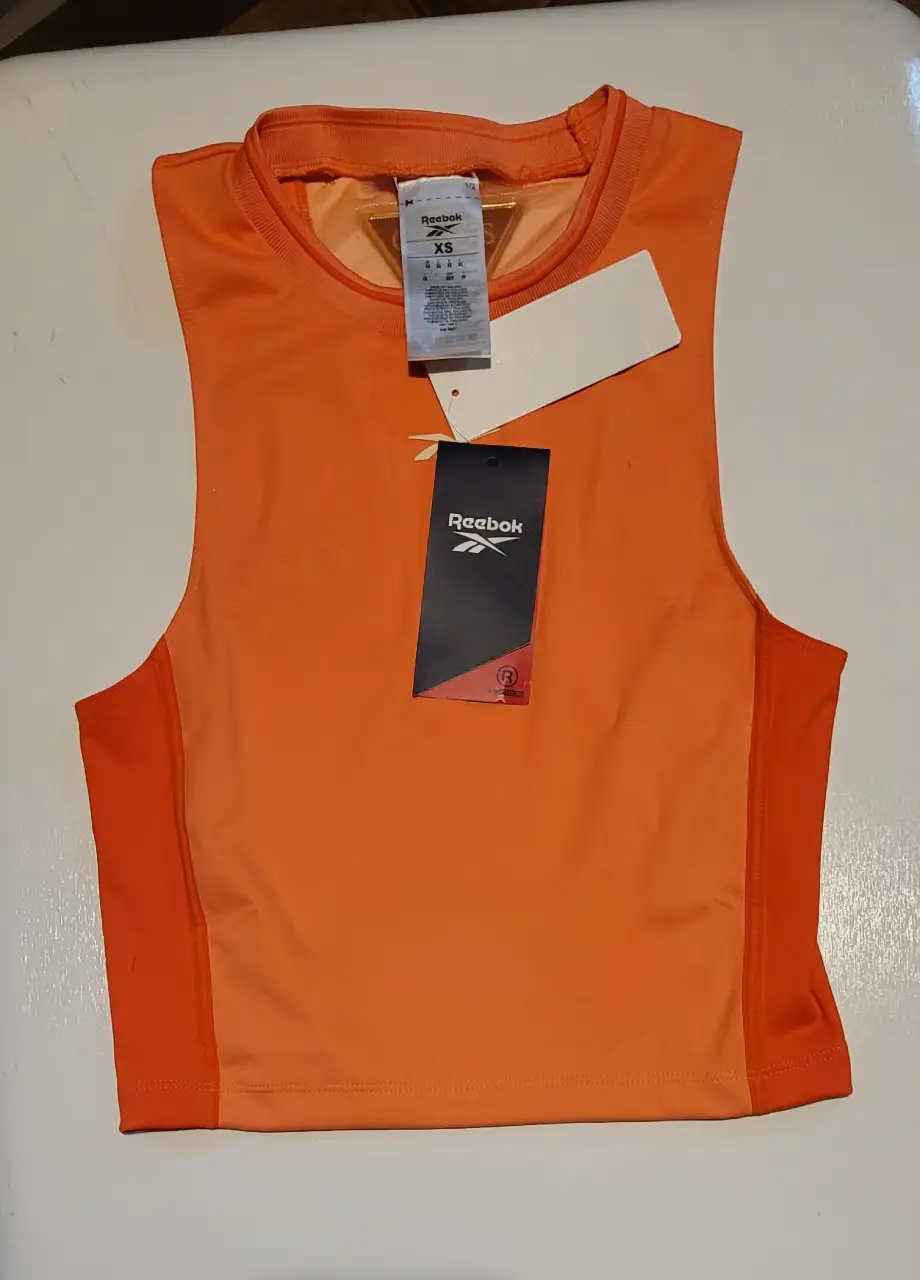 Musculosa deportiva Reebok naranja para mujer. Ideal para entrenamientos, con un diseño moderno y cómodo. Perfecta para actividades de verano.