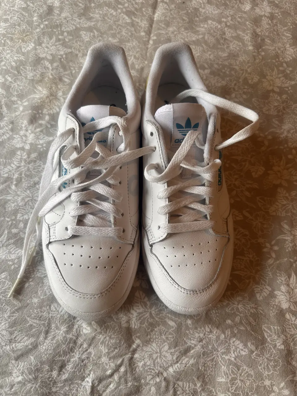 Zapatillas Adidas Continental 80 blancas, con detalles en celeste y amarillo. Ideales para un look casual y deportivo.