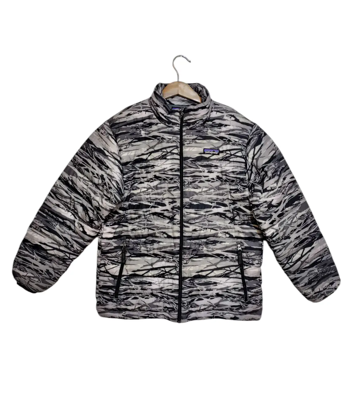 Campera de pluma Patagonia para niño, con estampado camuflado en tonos grises y negros. Posee cierre frontal, bolsillos con cierre y el logo de la marca en el pecho. Ideal para el invierno. Medidas: Largo 56 cm - Ancho sisa 45 cm.