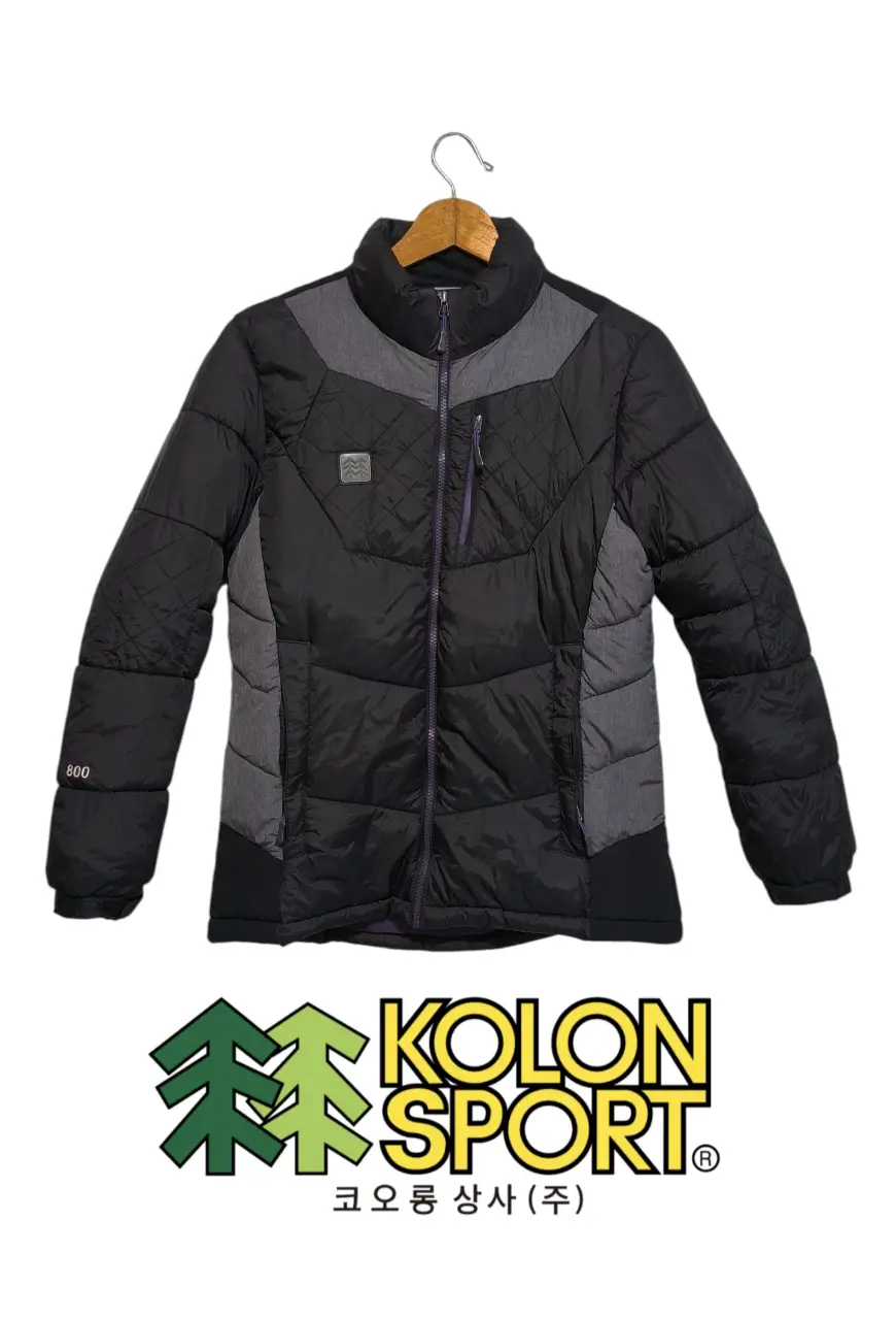 Campera de pluma negra y gris de la marca Kolon Sport 🇰🇷. Ideal para el invierno, con cierre y detalles en color violeta. Perfecta para actividades al aire libre. Solo le falta la capucha. Medidas: Largo 68 cm - Ancho 51 cm.
