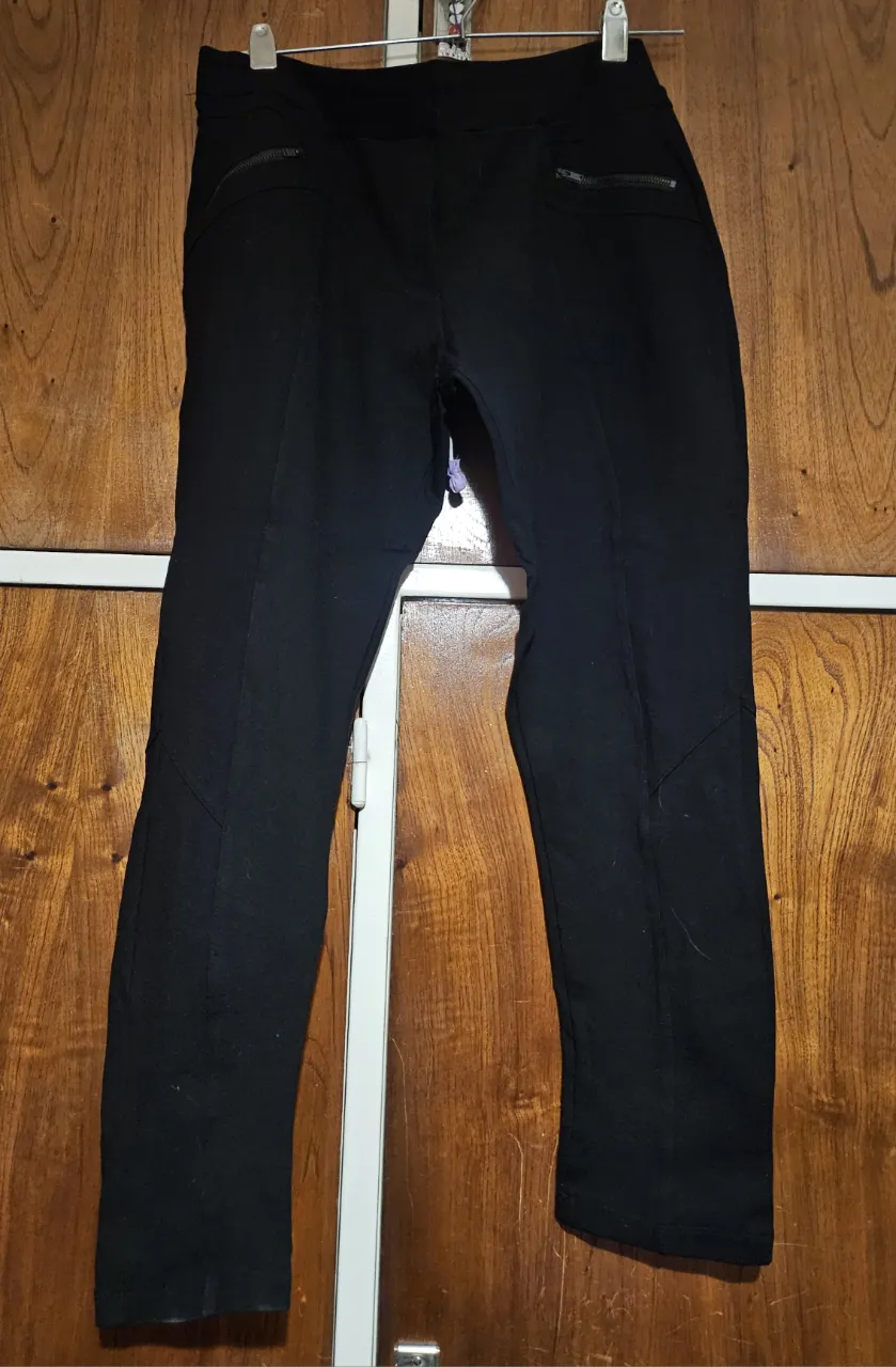Pantalón de vestir negro para mujer, con detalles de diseño en las costuras y bolsillos con cierre. Ideal para un look elegante y versátil.