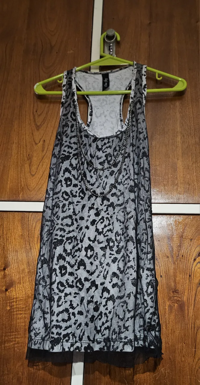 Musculosa de mujer con estampado de leopardo en tul negro sobre base blanca. Diseño de espalda deportiva y detalle de encaje en el borde inferior. Ideal para un look casual con un toque audaz.