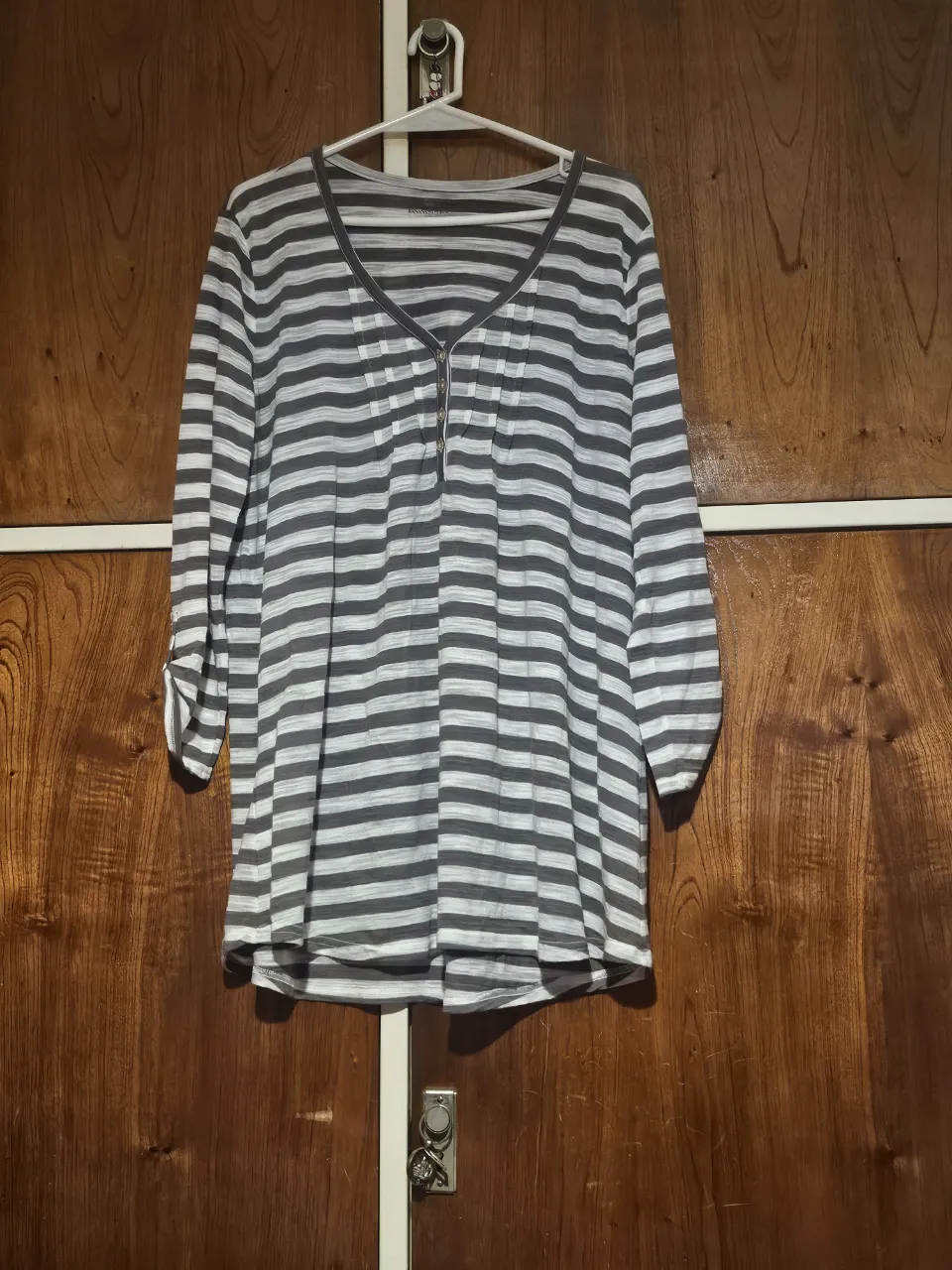 Blusa a rayas horizontales en gris y blanco, con mangas 3/4 y detalle de cierre en el cuello. Ideal para un look casual y cómodo.