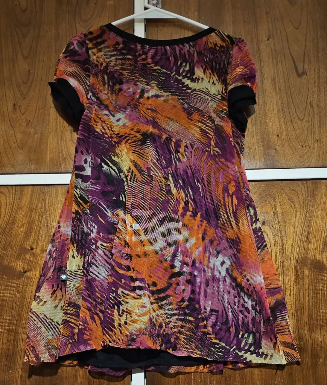 Vestido mini de mujer con estampado vibrante en tonos naranja, violeta y rosa. Diseño con mangas cortas y detalles en negro. Ideal para una salida o fiesta.