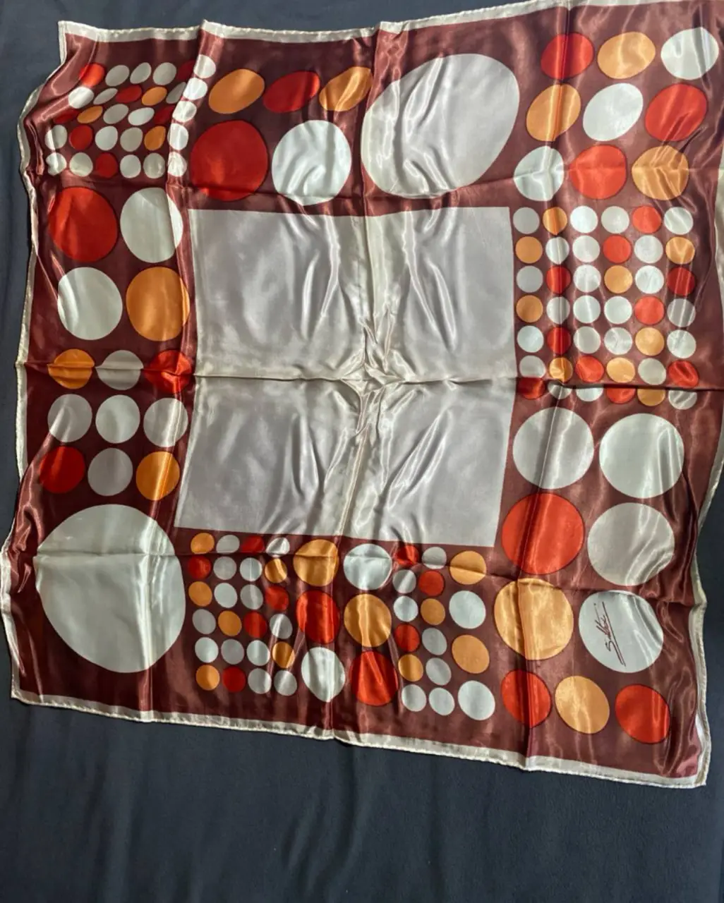 Pañuelo cuadrado de seda con estampado geométrico en tonos marrones, blancos y naranjas. Mide 85cm de cada lado