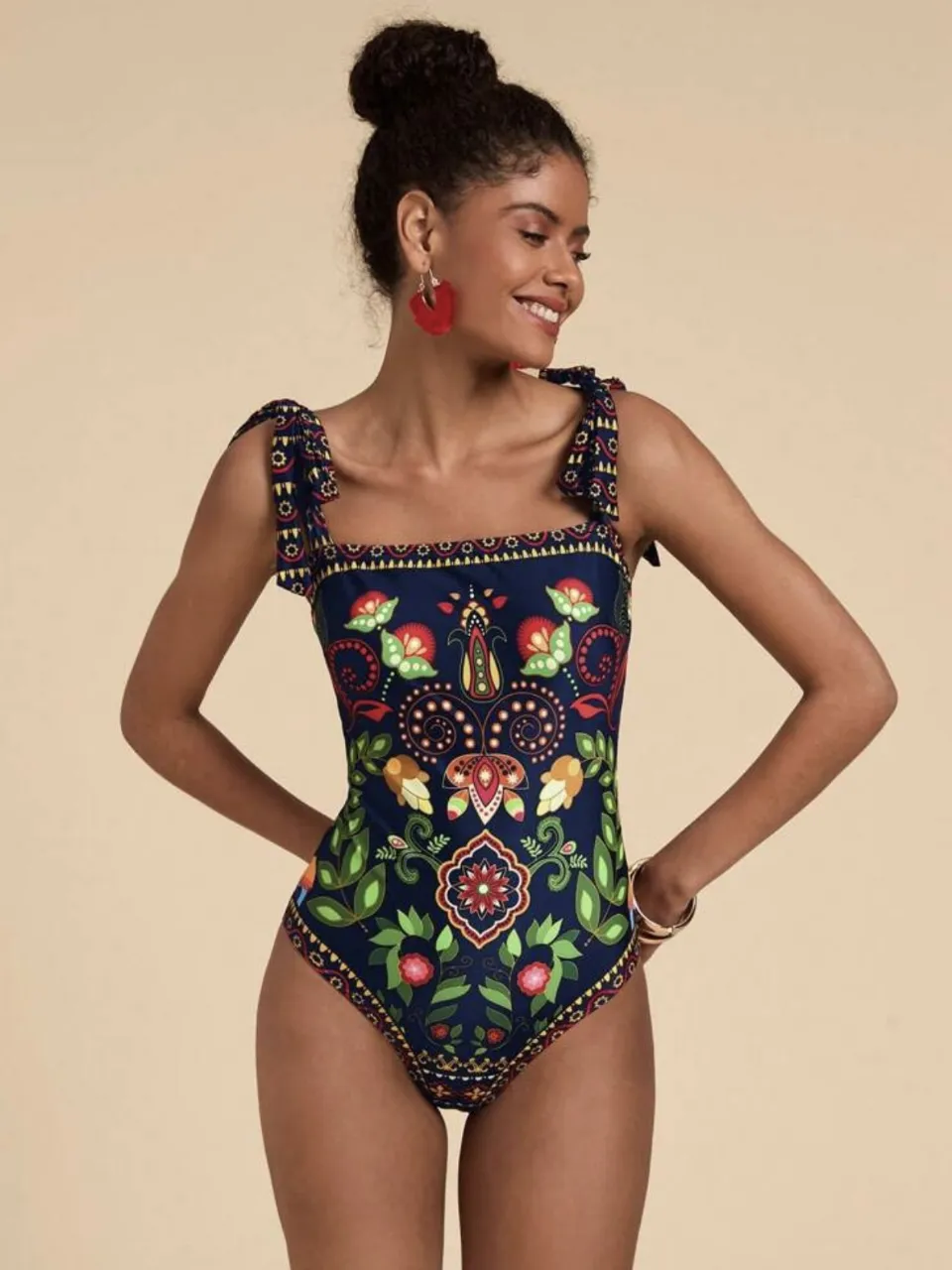 Traje de baño enterizo para mujer, con estampado floral en tonos azules, rojos y verdes. Diseño con tirantes anudados en los hombros y escote cuadrado. Ideal para lucir en la playa o piscina.