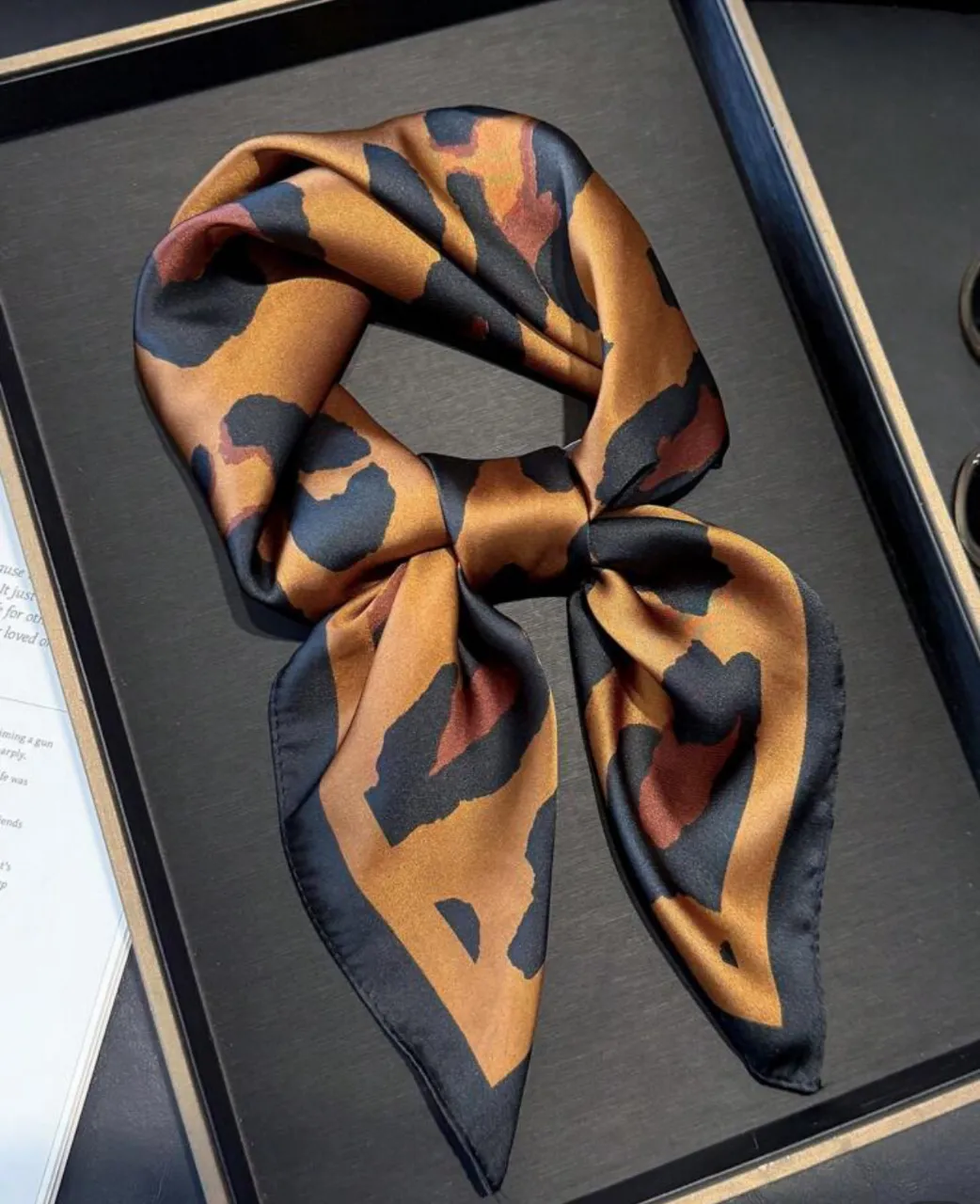 Pañuelo de seda con estampado de leopardo en tonos marrones y negros. Ideal para darle un toque de estilo a cualquier look. Perfecto para usar en el cuello, como accesorio para el pelo o atado a tu cartera.
