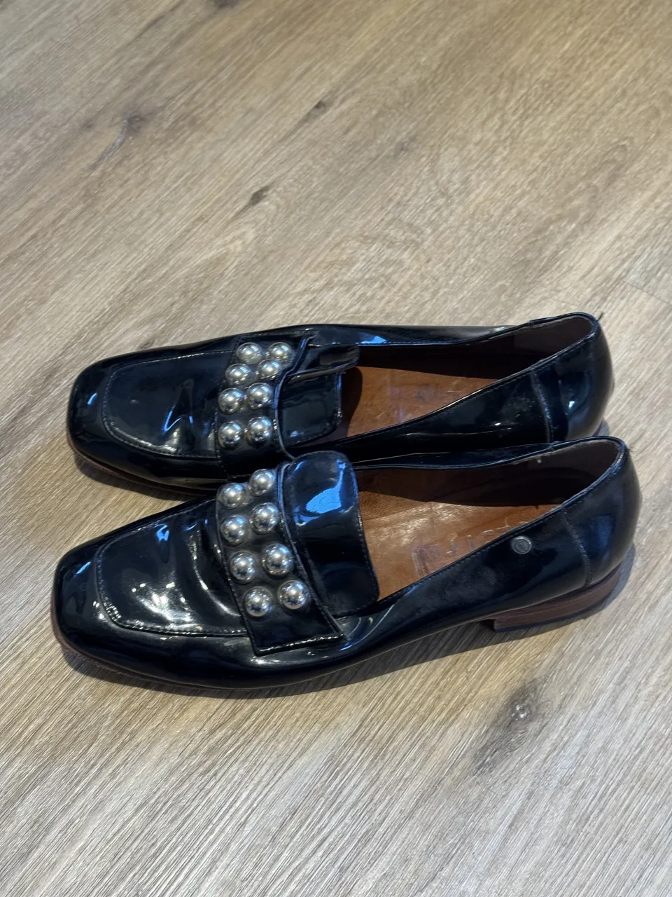 Zapatos negros de charol con detalle de tachas plateadas en la capellada. Suela de madera y goma.