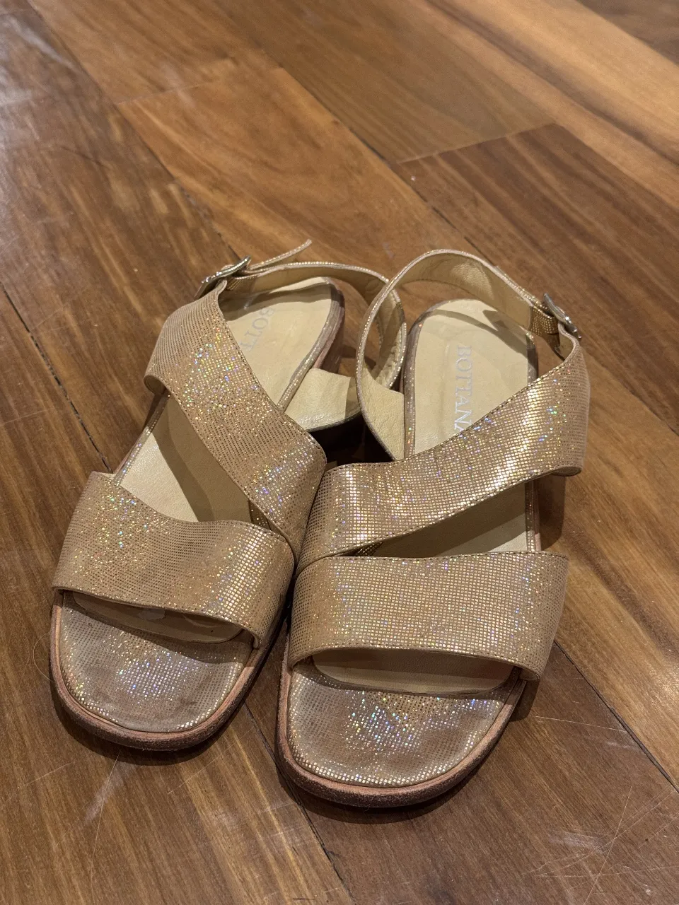 Sandalias doradas con brillo, ideales para un look de fiesta o salida. Con tiras cruzadas y hebilla ajustable.