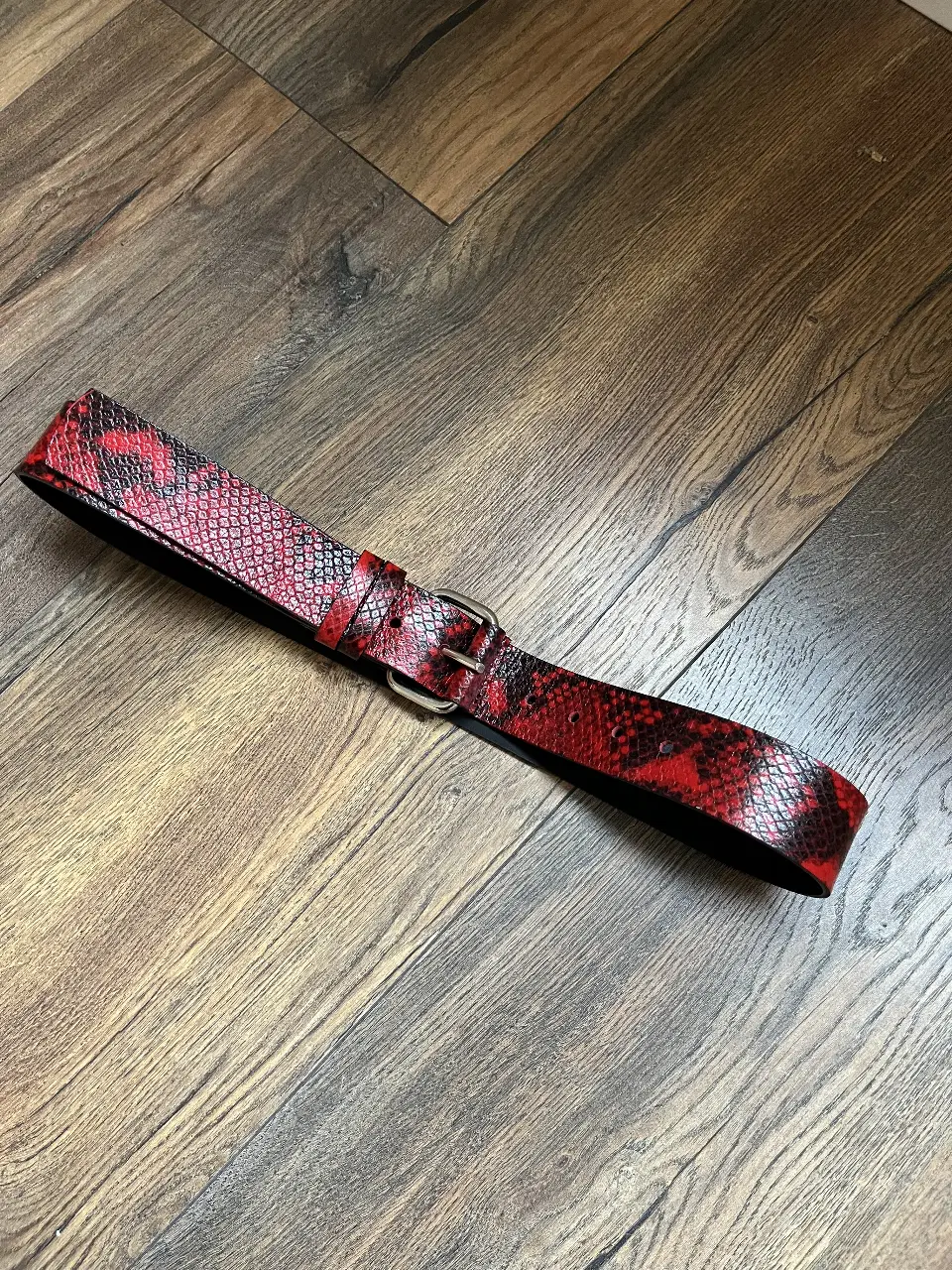 Cinturón de cuero con estampado de serpiente en tonos rojos y negros. Hebilla plateada. Ideal para darle un toque de estilo a cualquier outfit.