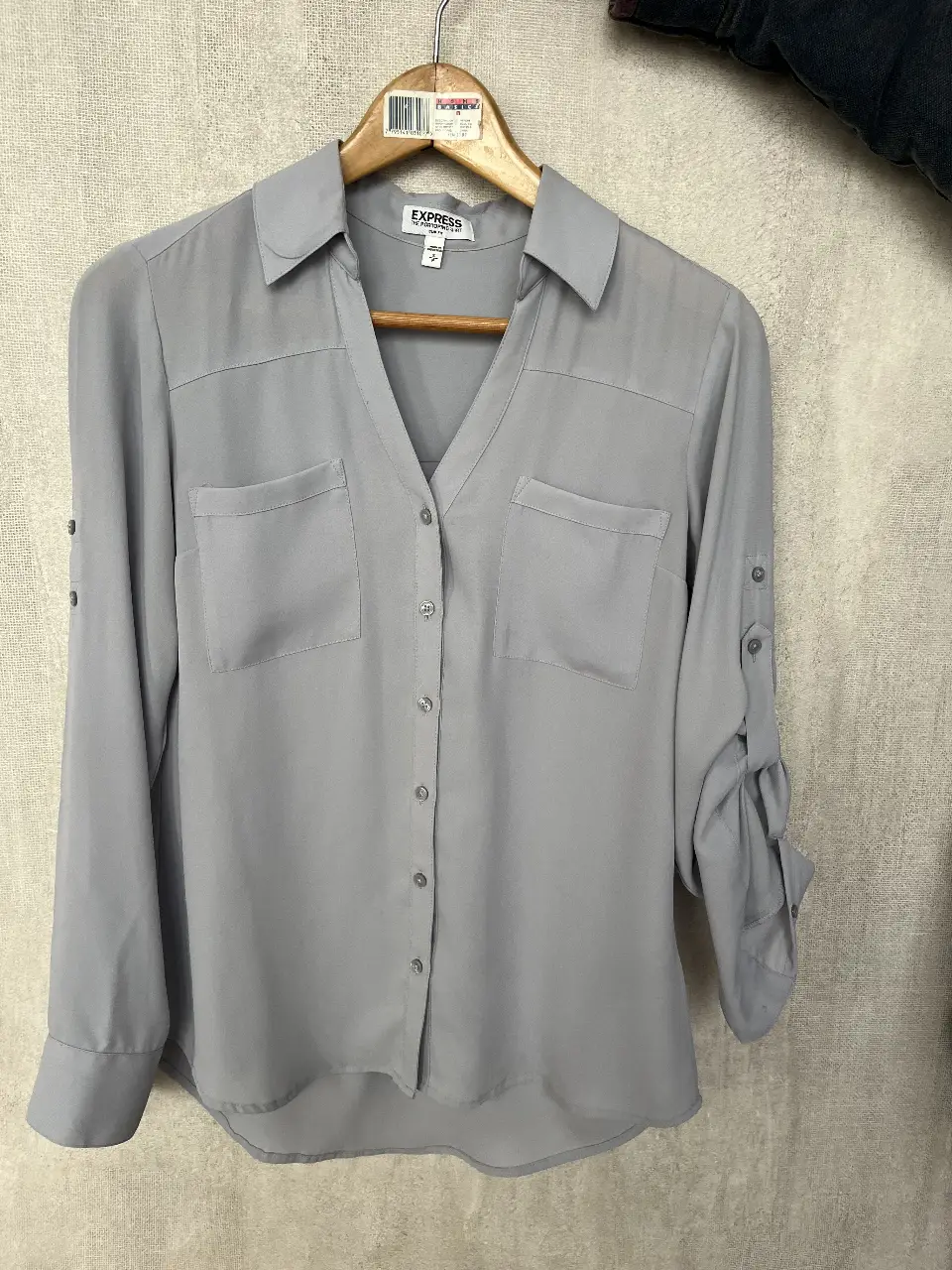 Camisa gris de la marca Express, modelo Portofino. Confeccionada en poliéster, de manga larga con detalle de botones para ajustar. Posee dos bolsillos delanteros y cuello camisero. Ideal para un look casual o de trabajo.