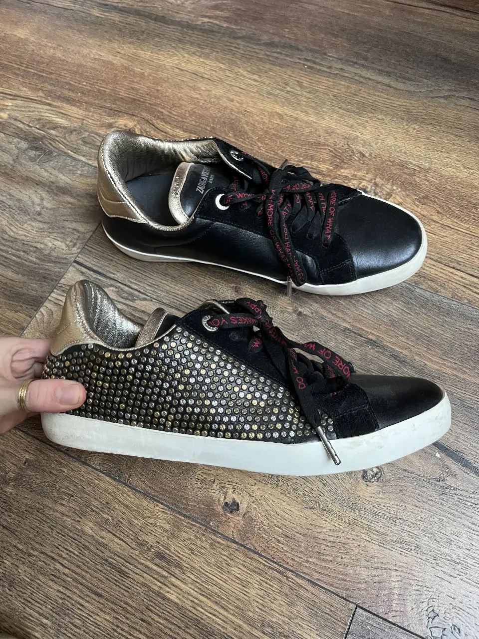 Zapatillas Zadig & Voltaire negras con detalles dorados y tachas. Cordones con frase. Suela blanca.