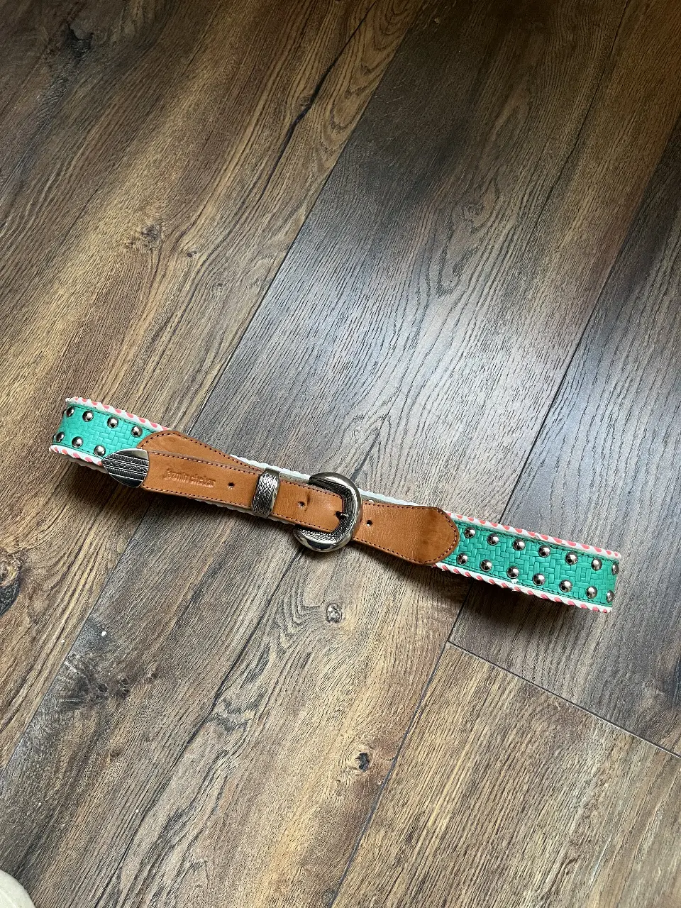 Cinturón de cuero con detalles en verde y plateado. Ideal para darle un toque de color a tus outfits.