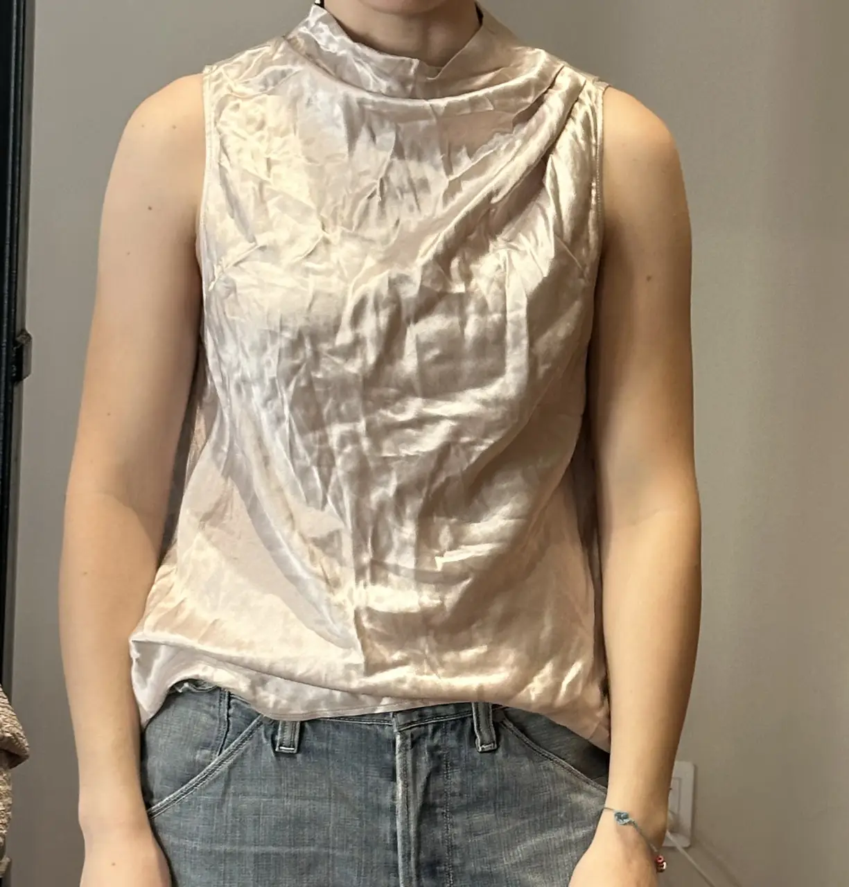 Blusa sin mangas de viscosa color crudo, con cuello alto y drapeado. Ideal para un look elegante y sofisticado.