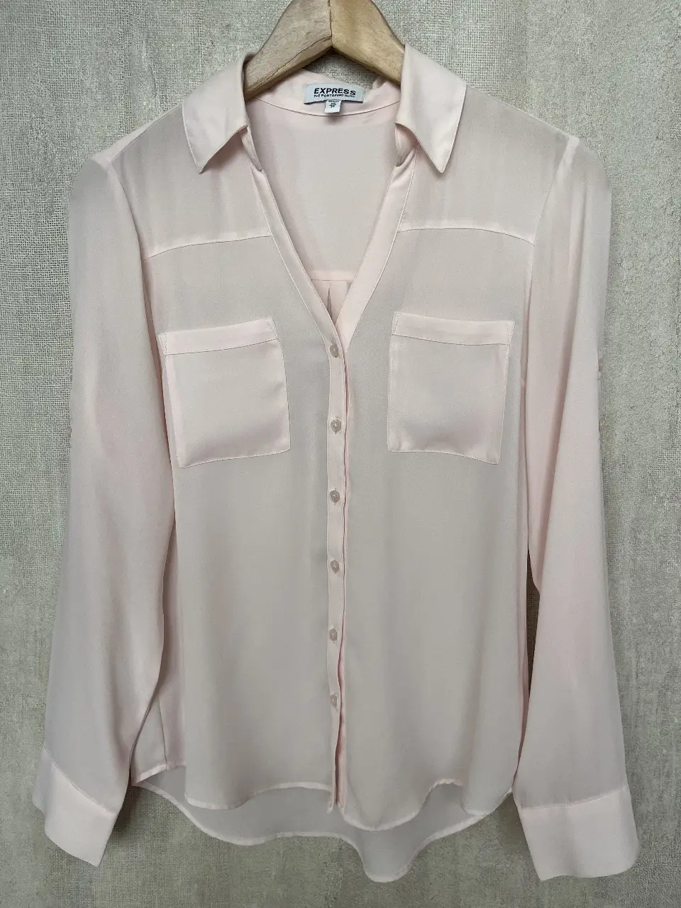 Blusa de la marca Express, modelo Portofino, en color rosa claro. Confeccionada en poliéster, esta camisa de manga larga presenta un diseño elegante con dos bolsillos delanteros y botones. Ideal para un look casual o de trabajo.